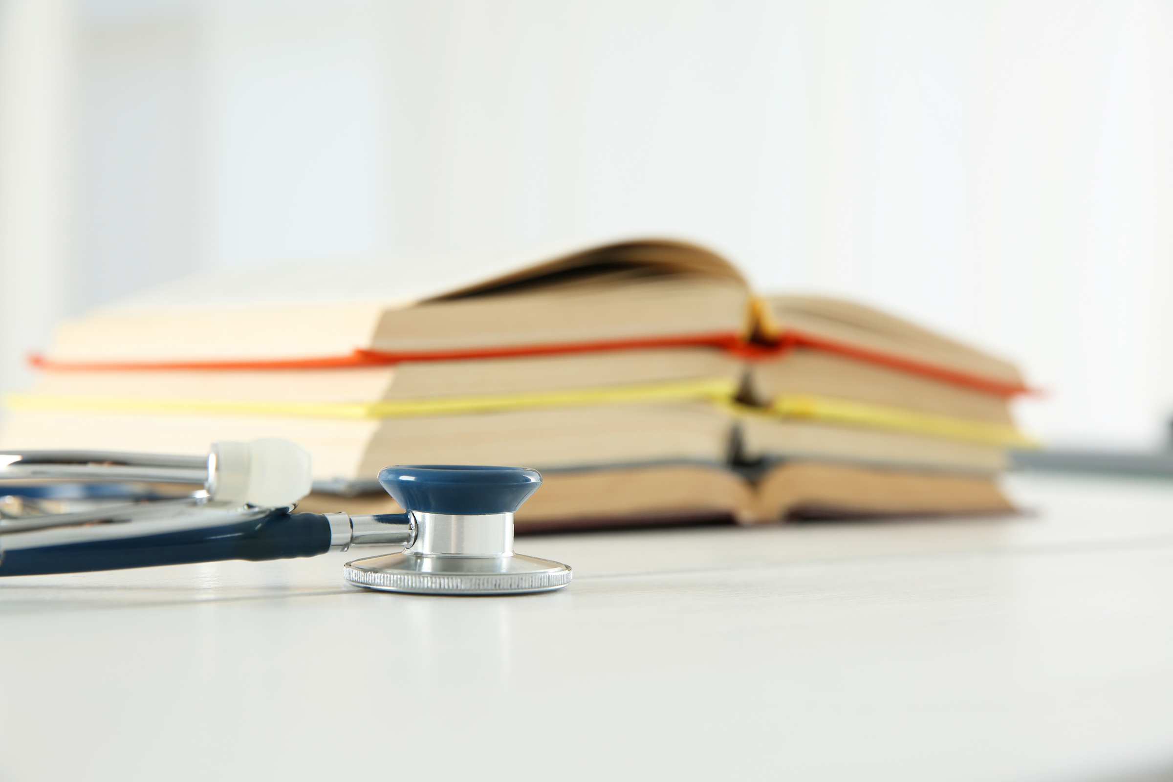A stethoscope beside medical reference books on a desk.