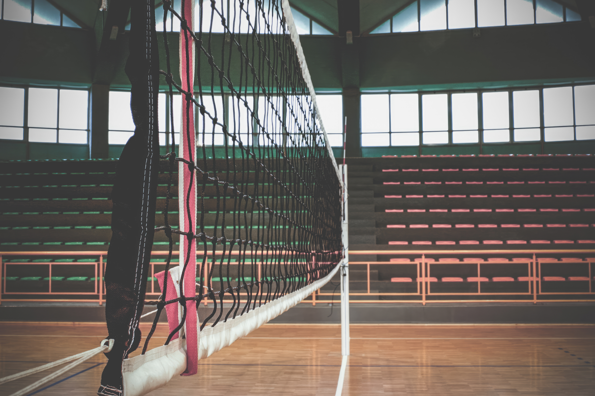 Empty indoor volleyball court with a net and wooden floor.