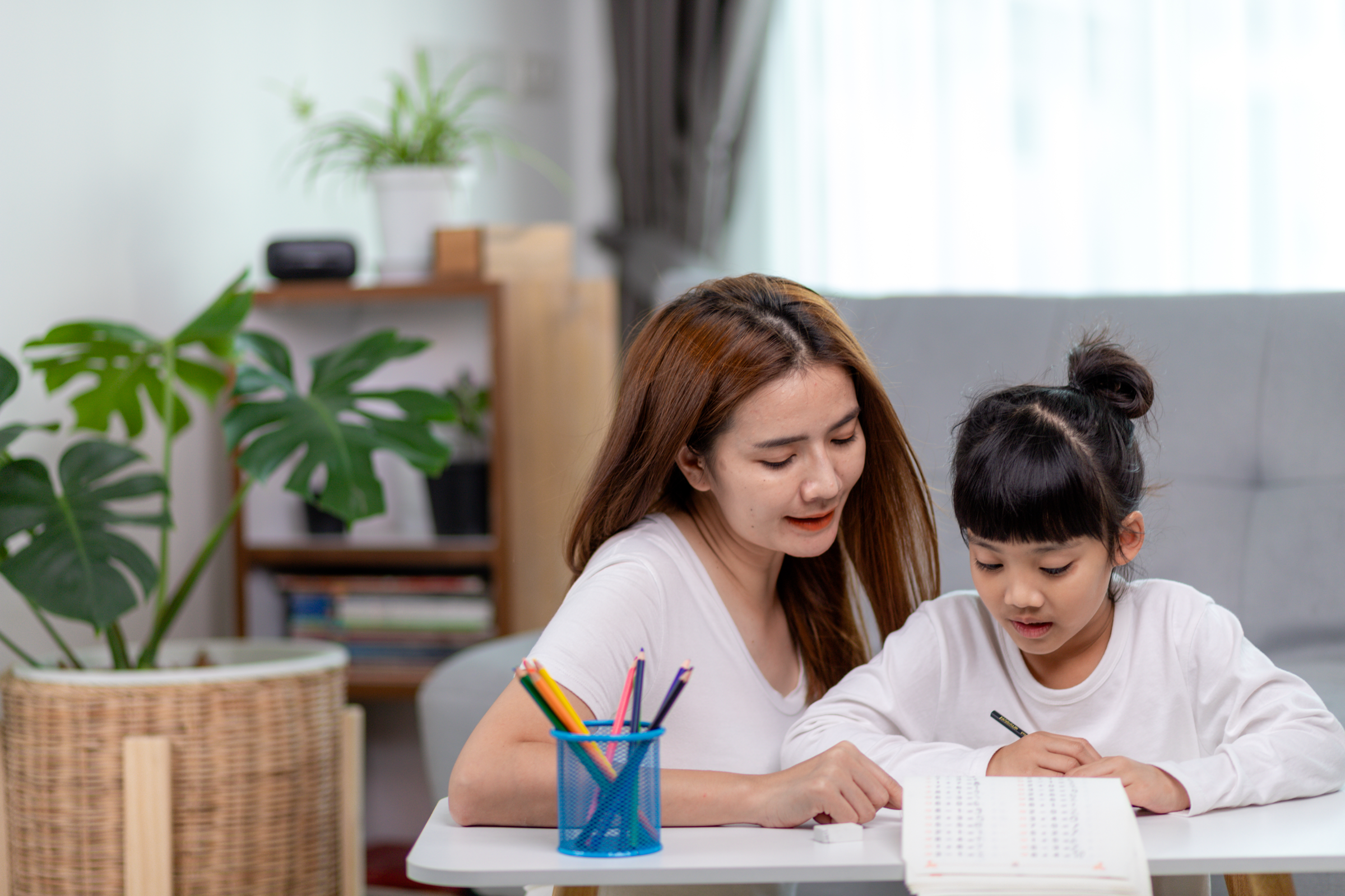 A woman helping a girl with schoolwork at a table.