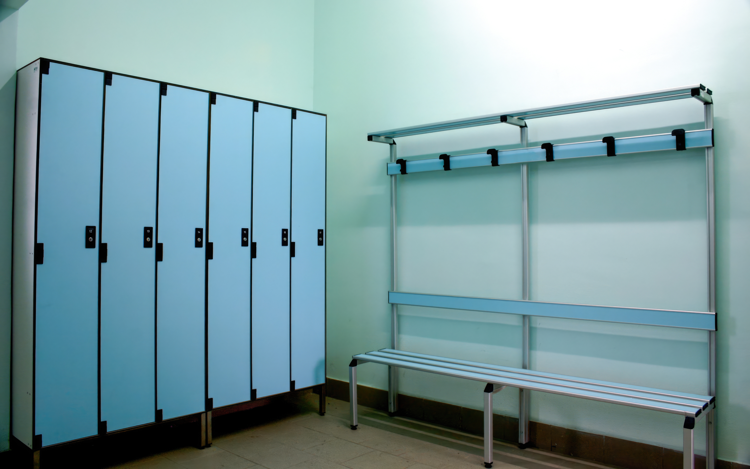 Blue lockers and a bench in an empty athletic locker room.