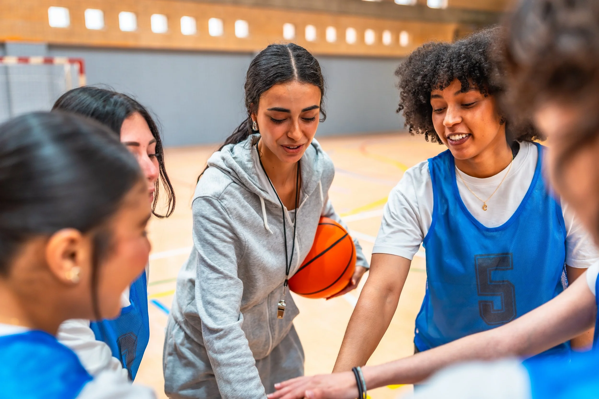 Female basketball players and their coach huddling together on an indoor court.