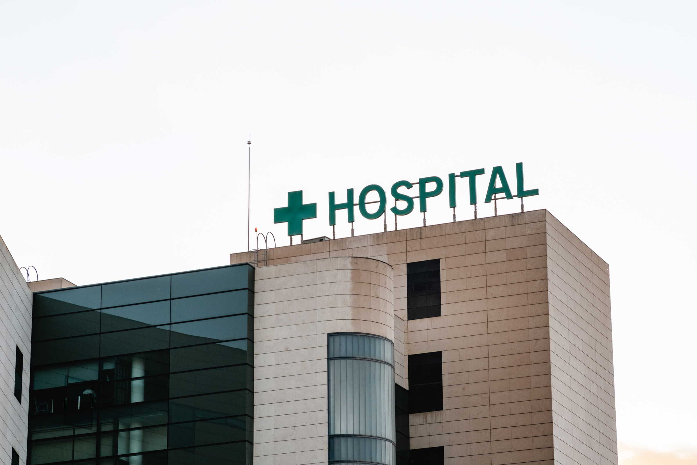 Hospital exterior with a green cross and hospital sign.