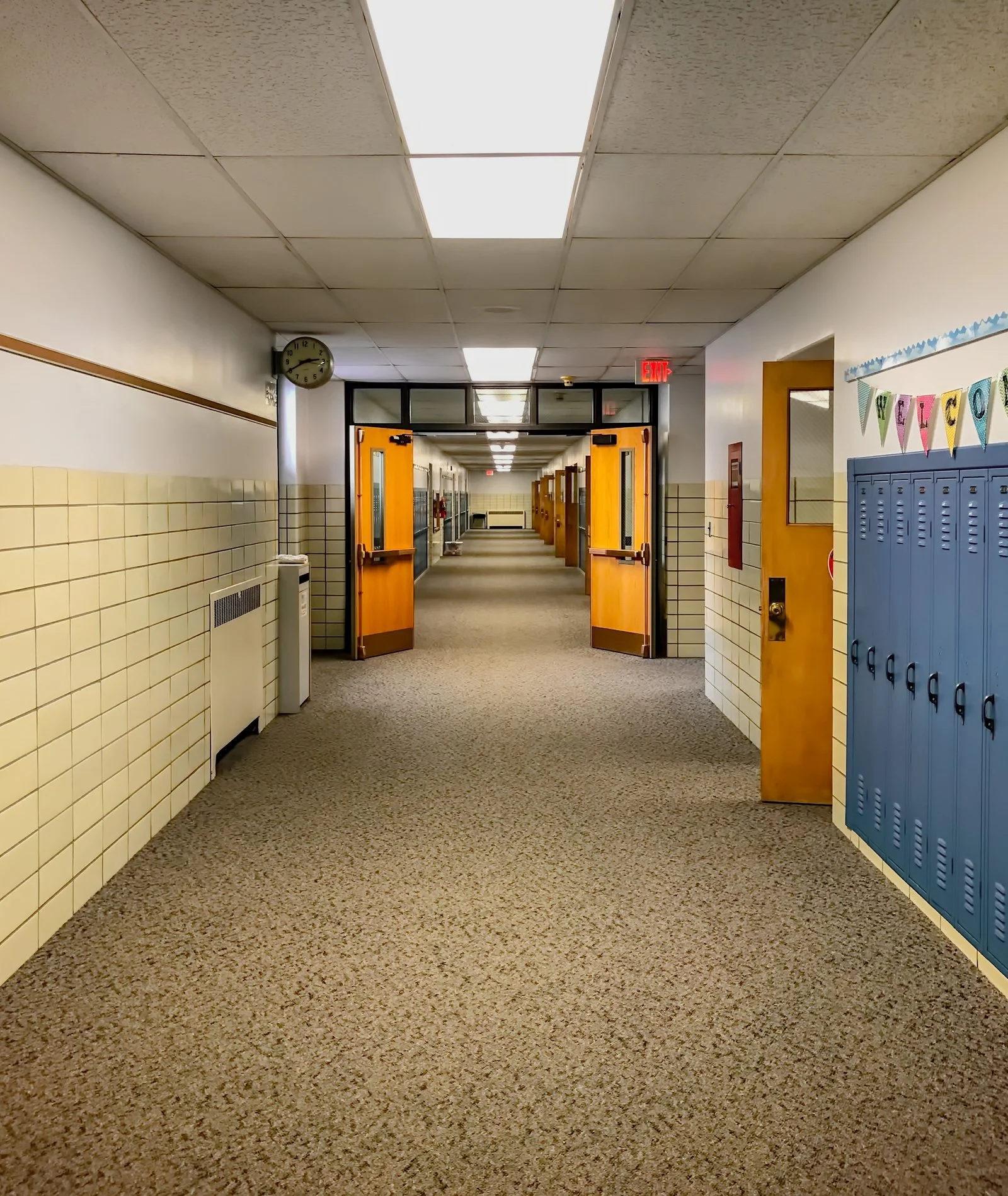 Empty school hallway with blue lockers and open classroom doors.
