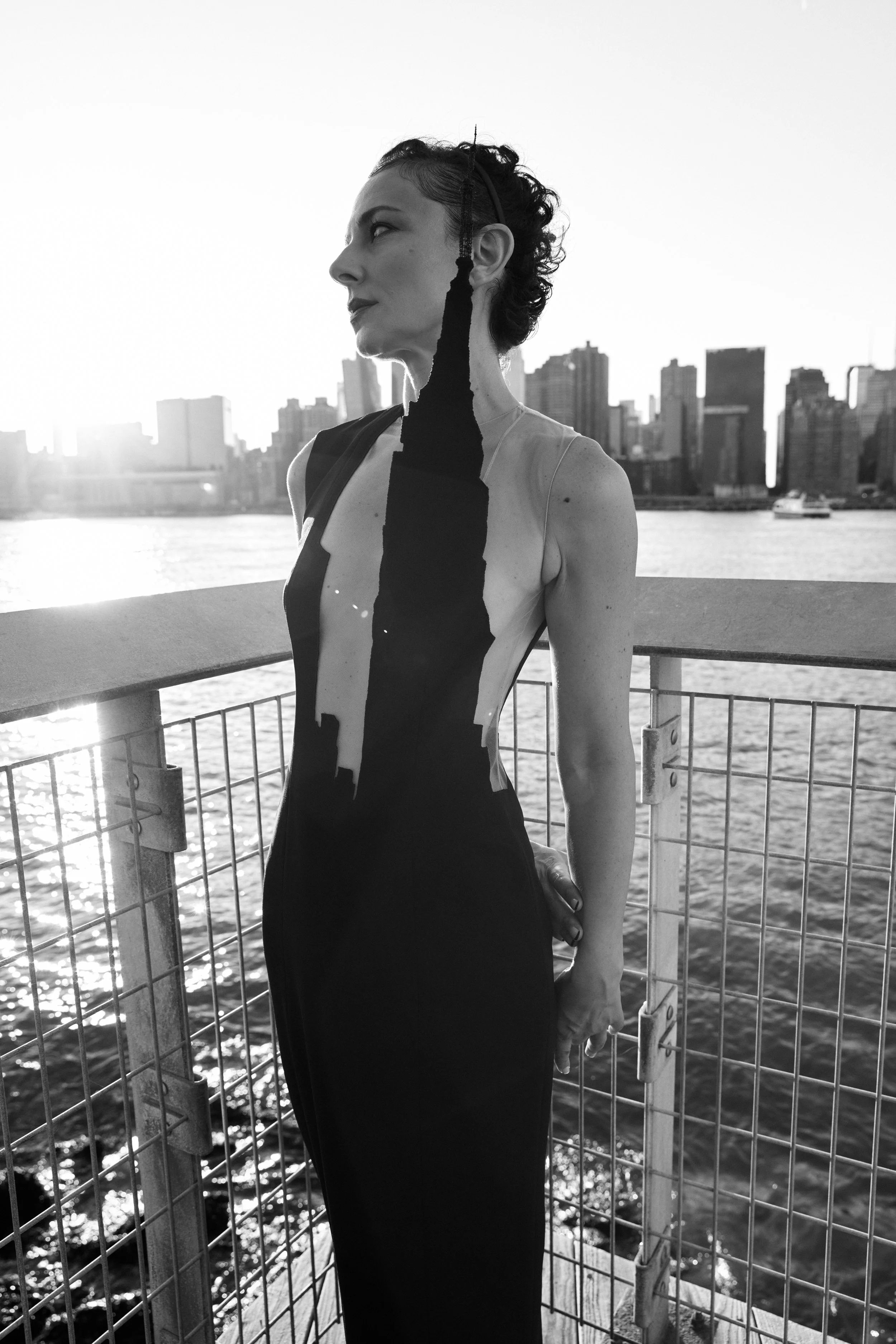 Nicky Conti in a sculptural black couture look inspired by the silhouette Empire State Building, standing at Gantry Plaza Park with Manhattan in the background