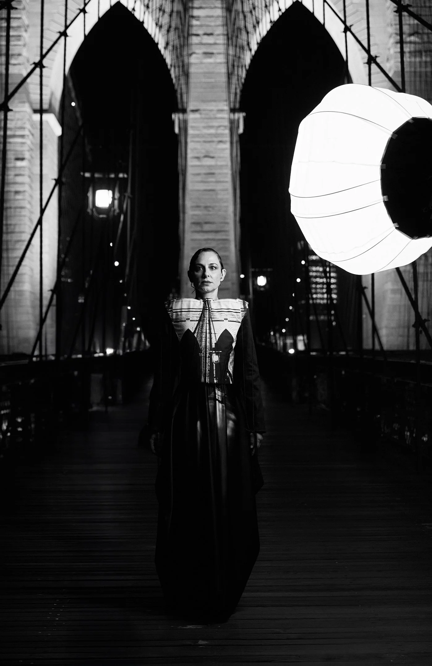 Nicky Conti wearing the Robe-ling couture look on the Brooklyn Bridge at night, with a lantern used during the photoshoot visible in the corner
