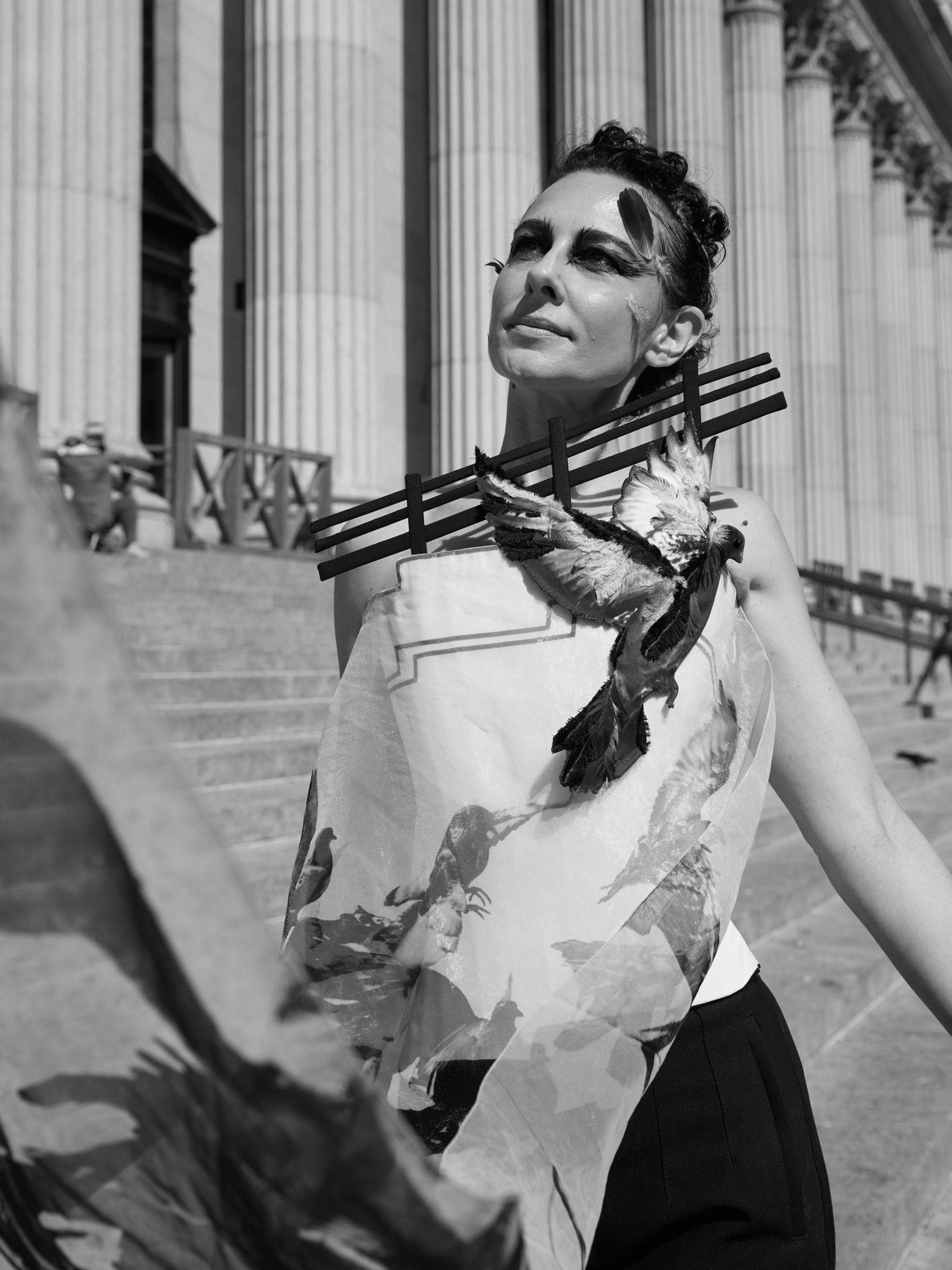 Nicky Conti wearing the Adaptress look on the James Farley Building stairs, looking upward as pigeons fly nearby, with a structured corset and printed organza overlay