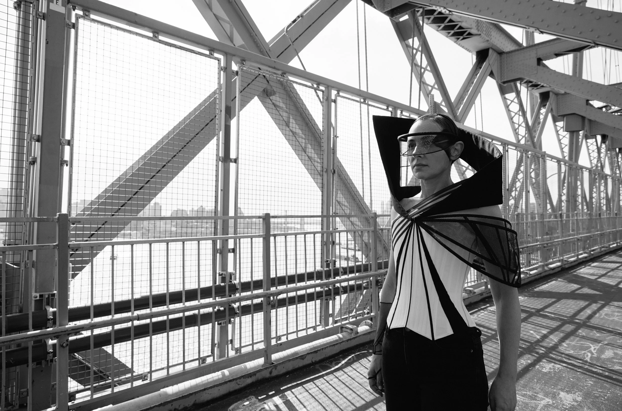 Nicky Conti walking along the Williamsburg Bridge in the Ironick couture piece, with a fitted corset, mesh and boning on one arm, and a headpiece echoing the bridge’s arch
