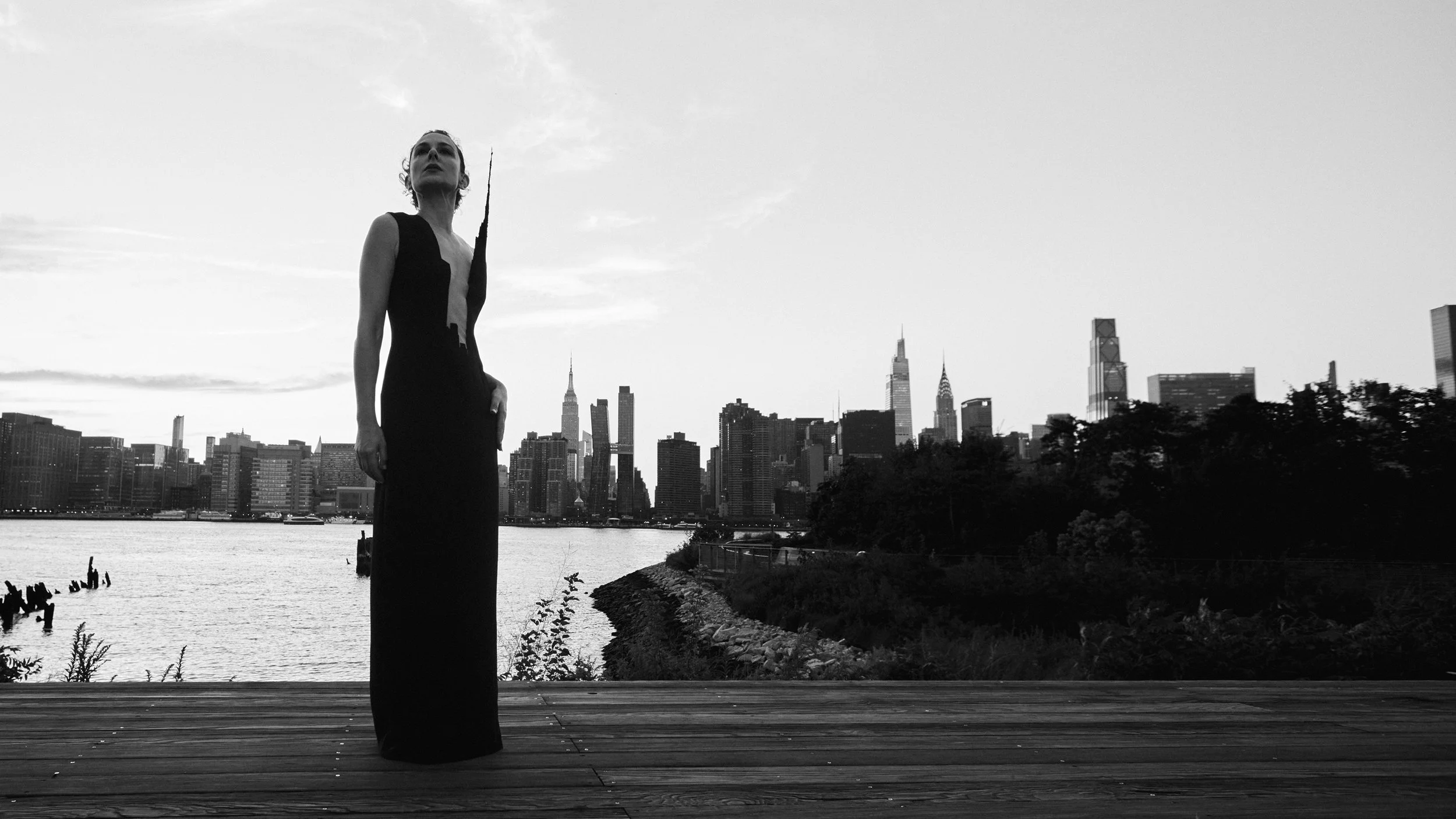 Nicky Conti wearing the Empeiria architectural couture dress with the Manhattan skyline and Empire State Building in the background, photographed at Gantry Plaza Park in New York City