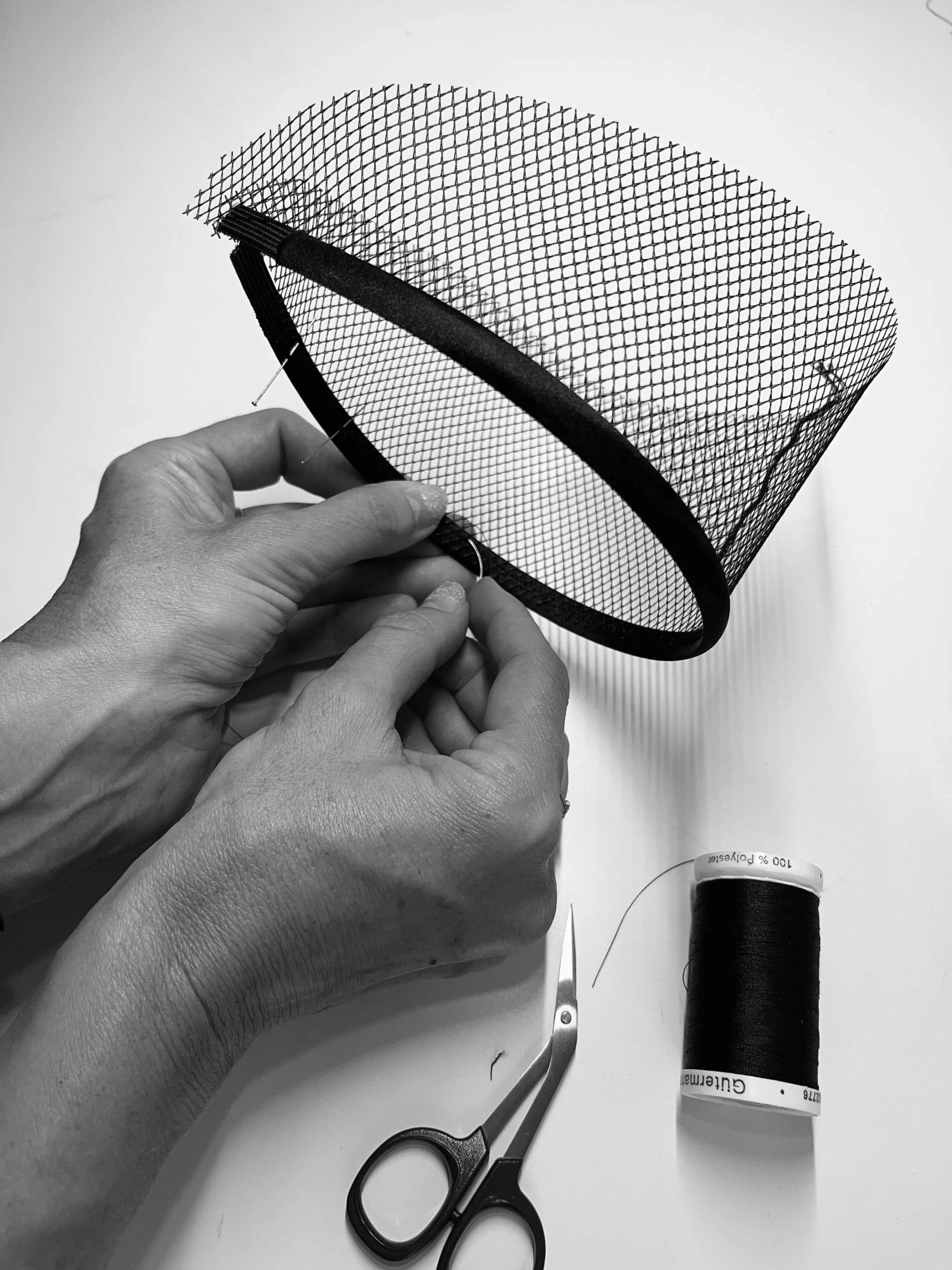 Hands of textile artist Sarah Esmoingt shaping a mesh face mask with black ribbon piping, carefully constructing the structured piece that completes the Ironick look.