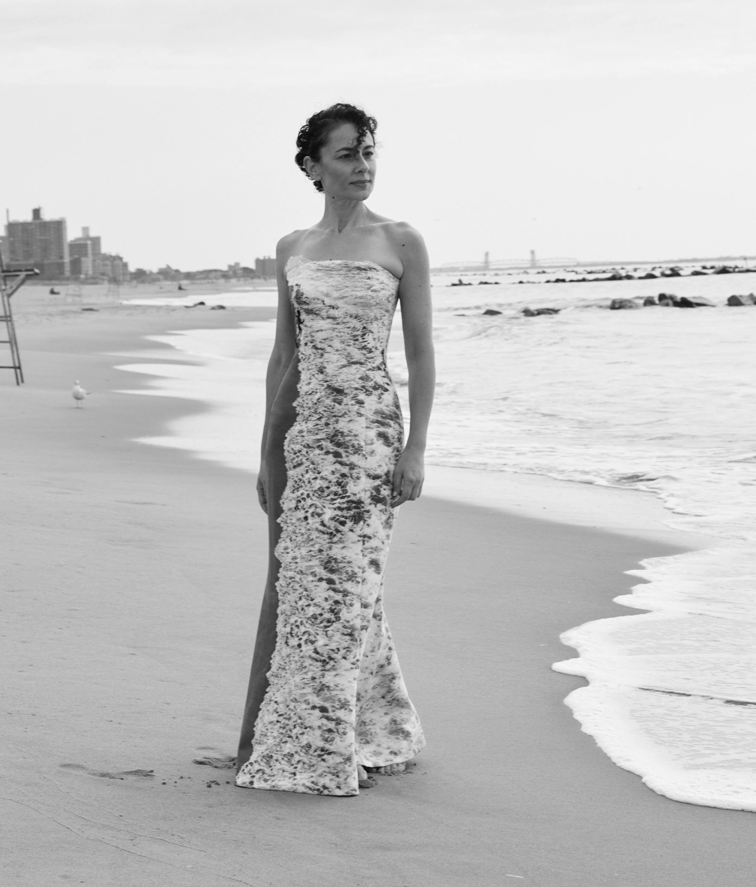 Nicky Conti walking along the shoreline at Coney Island Beach wearing the Memoria couture dress looking out toward the water