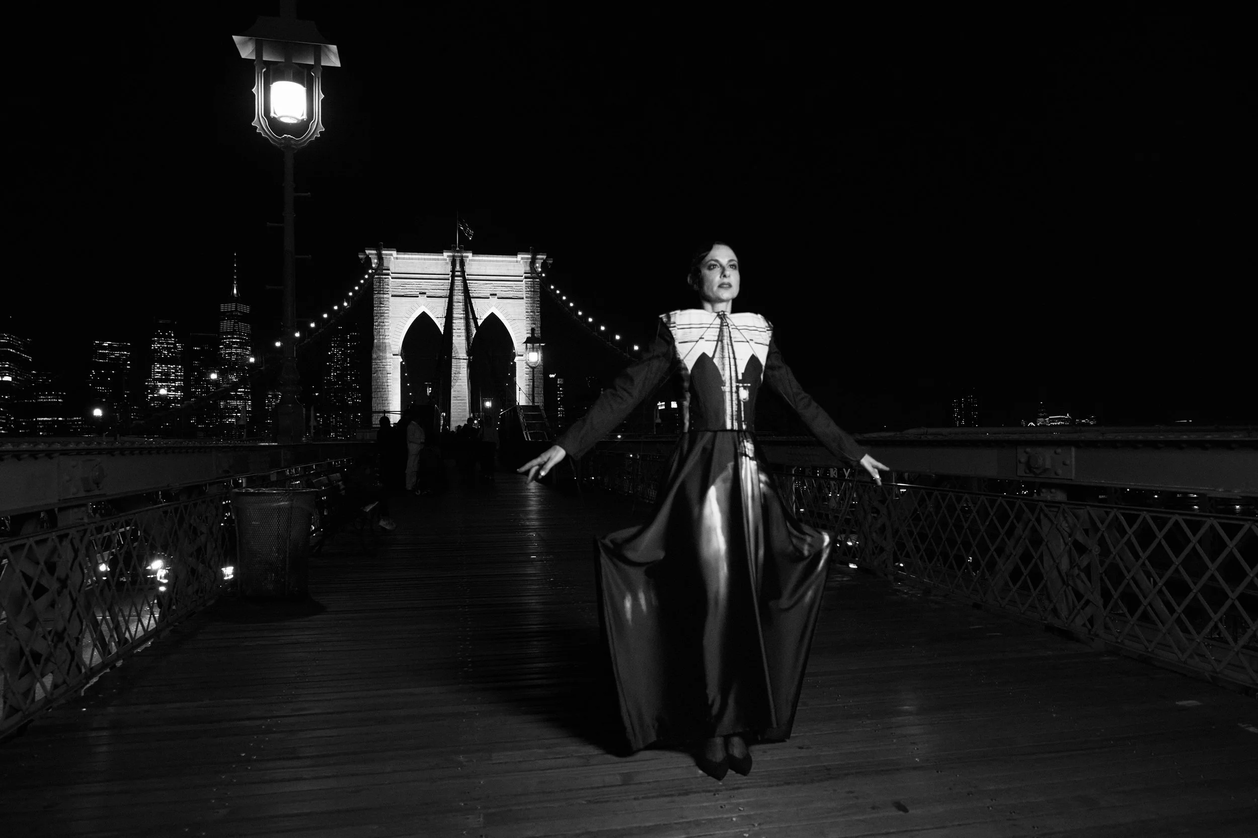 Nicky Conti in architectural piece with chain elements, standing on the Brooklyn Bridge at night
