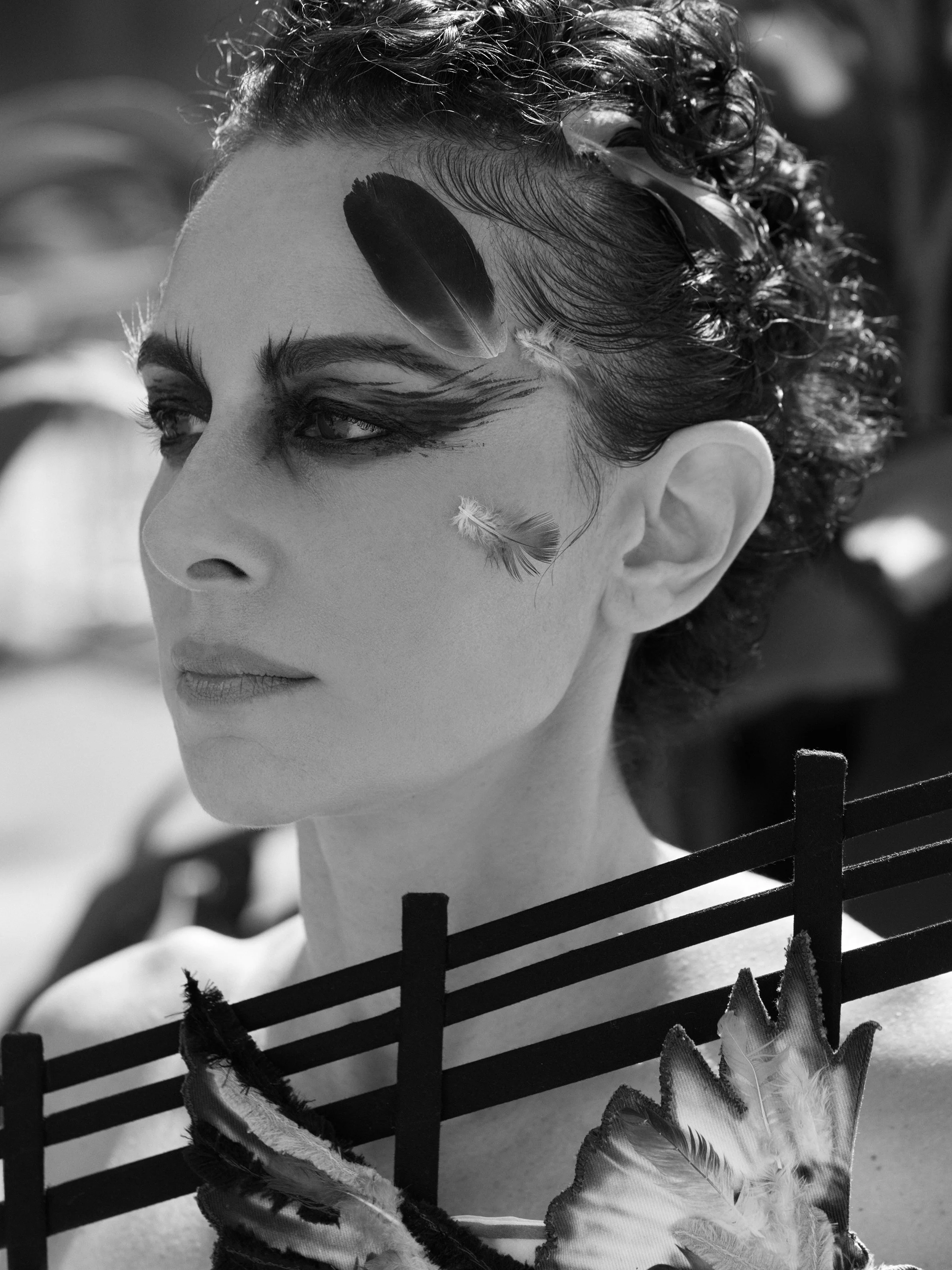 Close-up of Nicky Conti wearing feathers in her hair and on her face as part of the Adaptress look, with a pigeon motif visible on the garment
