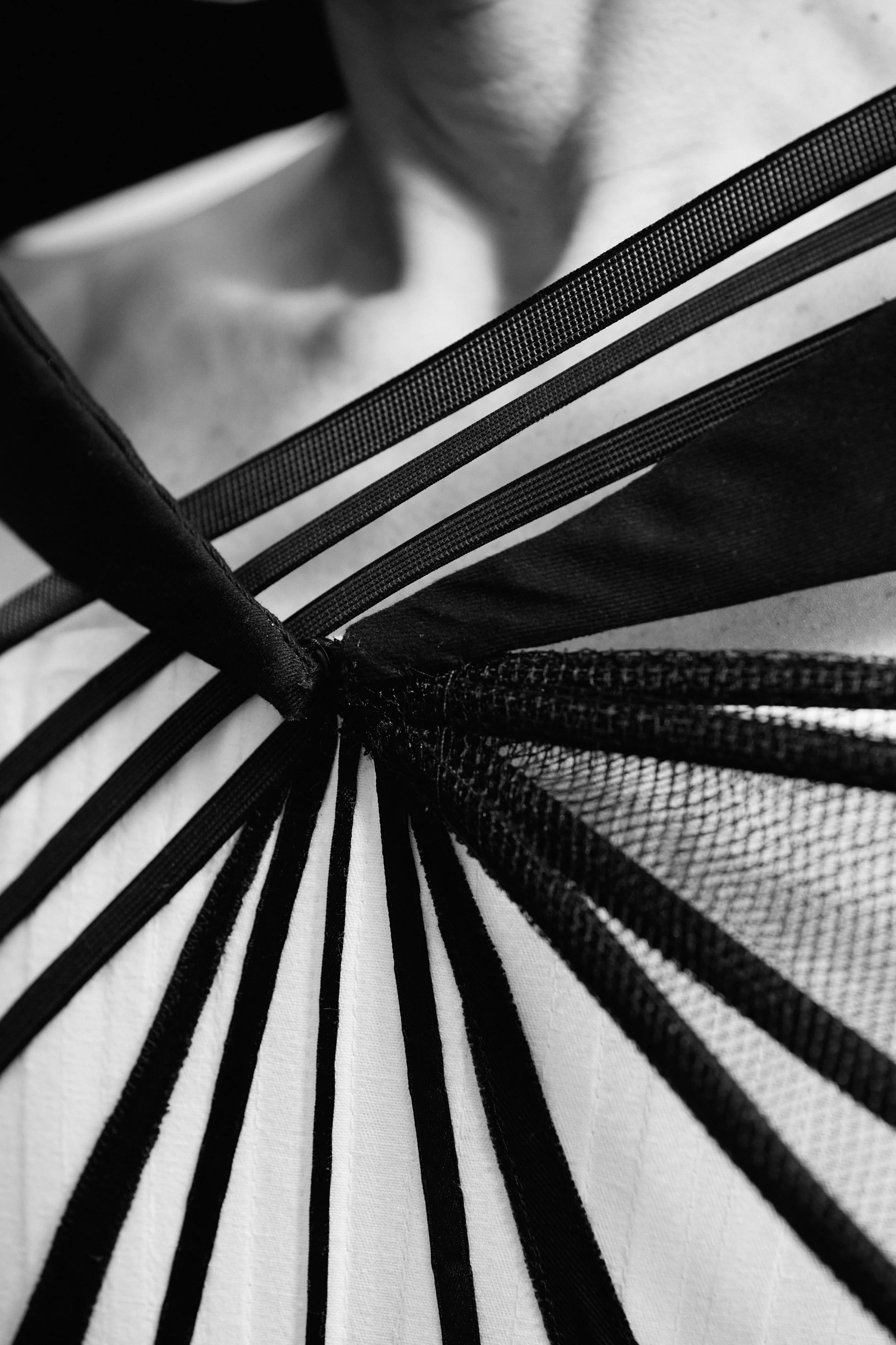 Close-up of a white corset with black ribbons and boning running diagonally across the bodice, creating a structured, geometric pattern inspired by the steel lines of the Williamsburg Bridge.