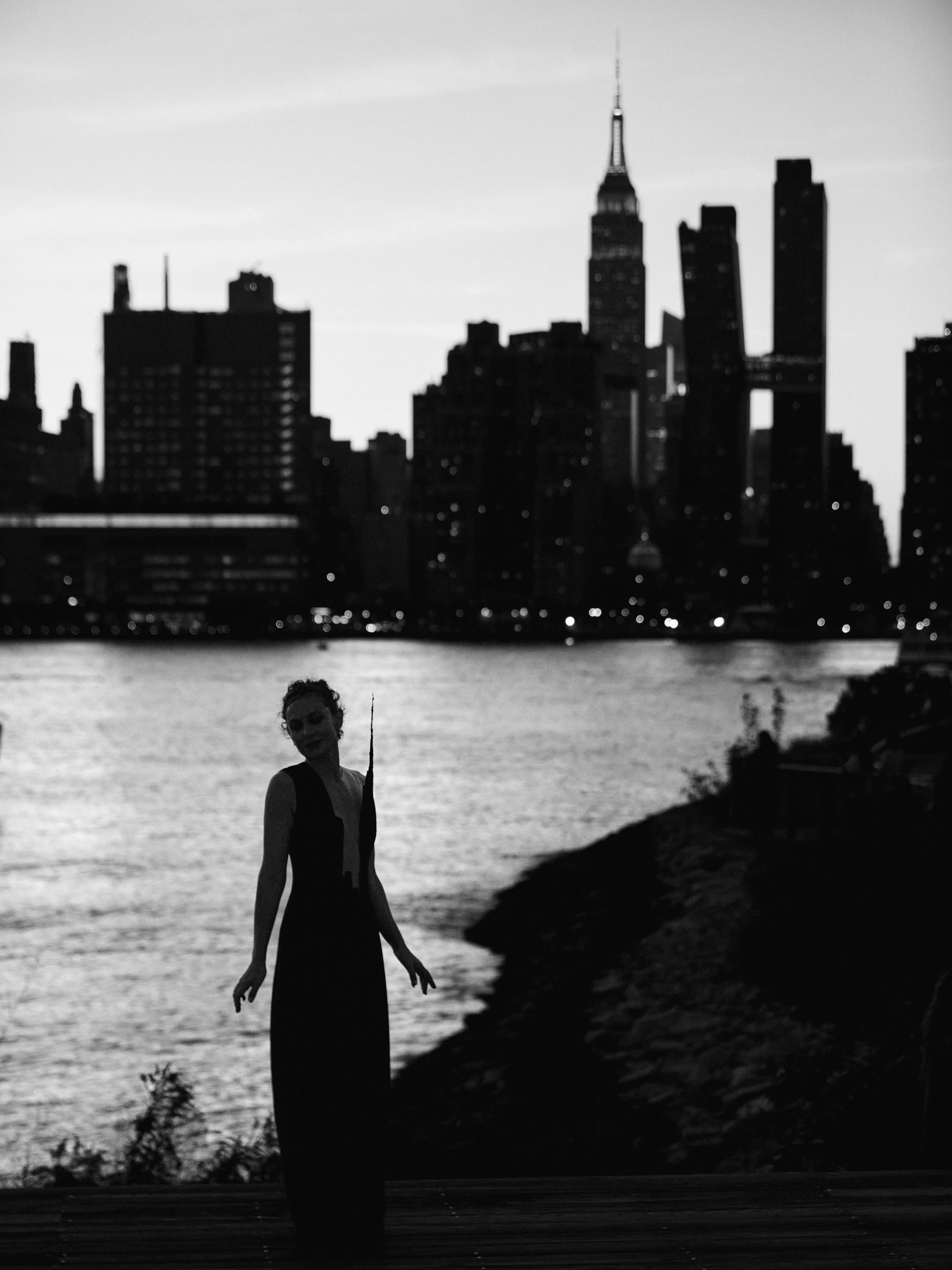 Silhouette of Nicky Conti wearing the Empeiria custom-made couture dress against a sunset sky at right at the time the original photo of the Empire State Building was taken