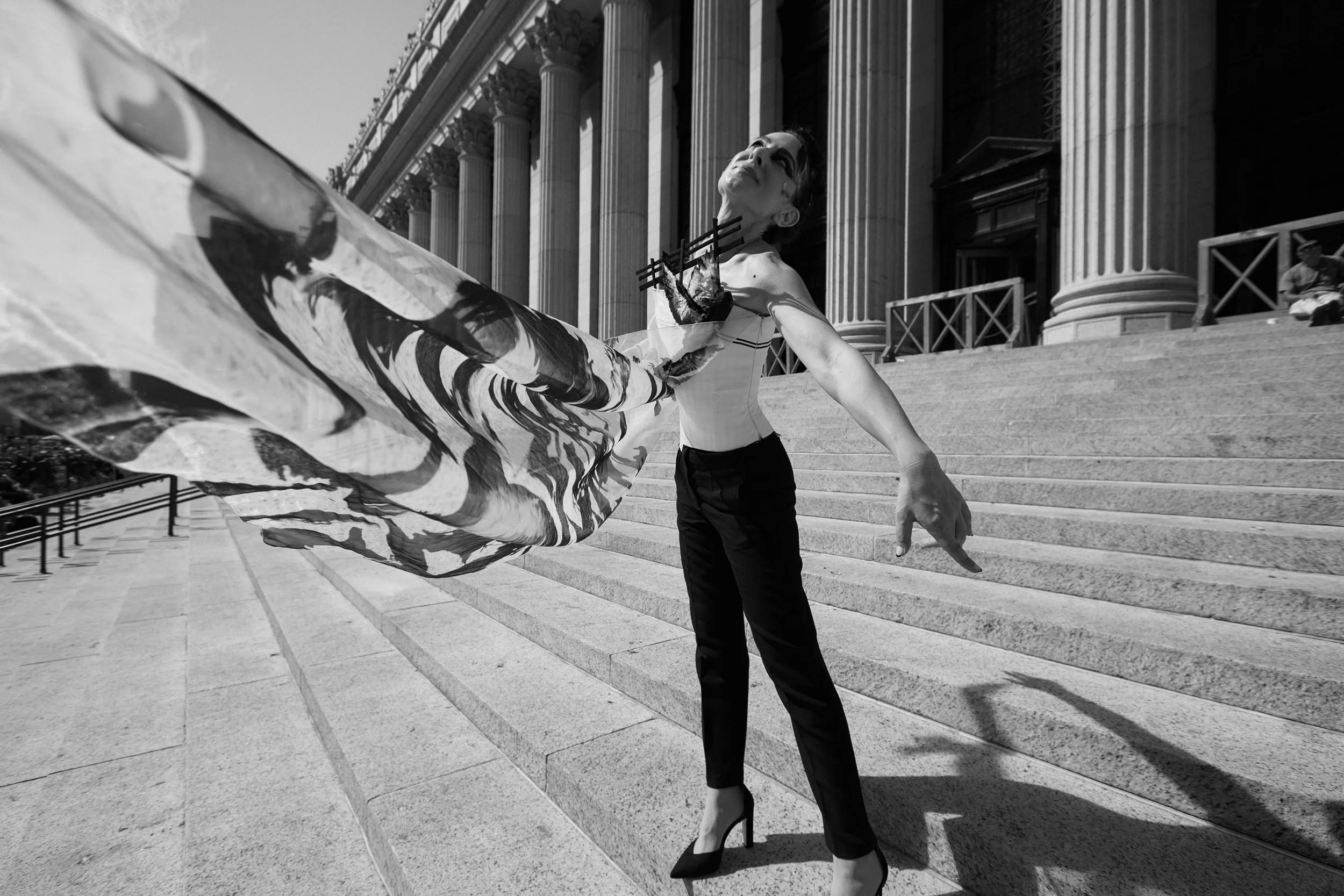 Nicky Conti posing on the stairs of the James Farley Building, imitating the flight of pigeons while wearing the Adaptress couture look with feather details and flowing organza