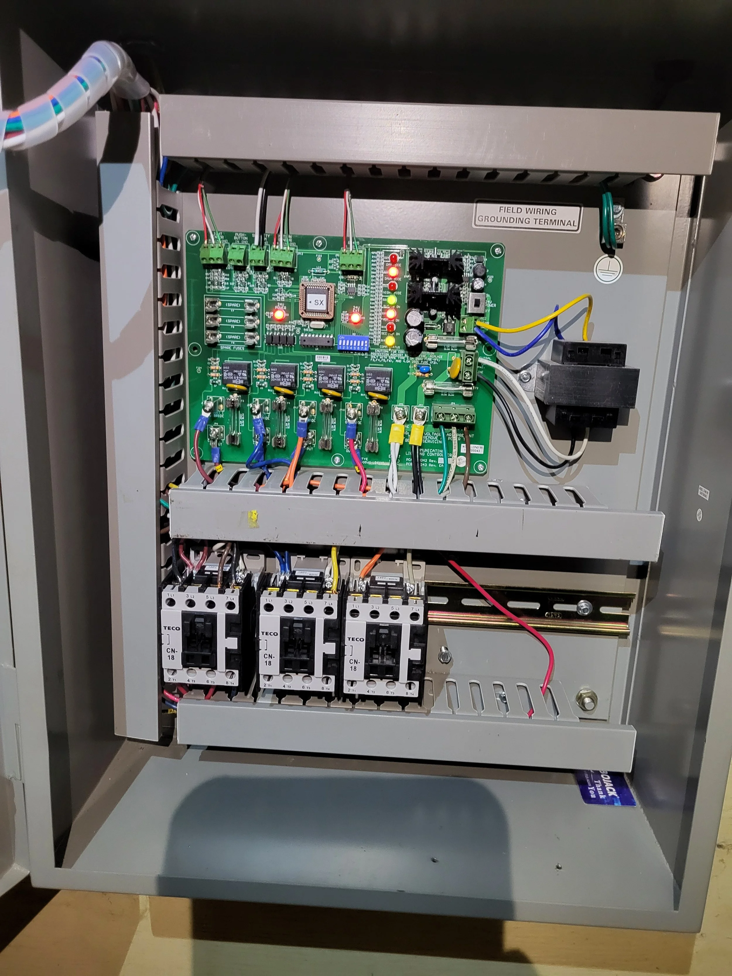 Electrical control panel with circuit boards, wiring, and relays inside a gray metal enclosure.