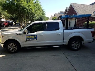 Silver pickup truck with a Burdham Electric sign on the door, parked under a tree on a residential street.