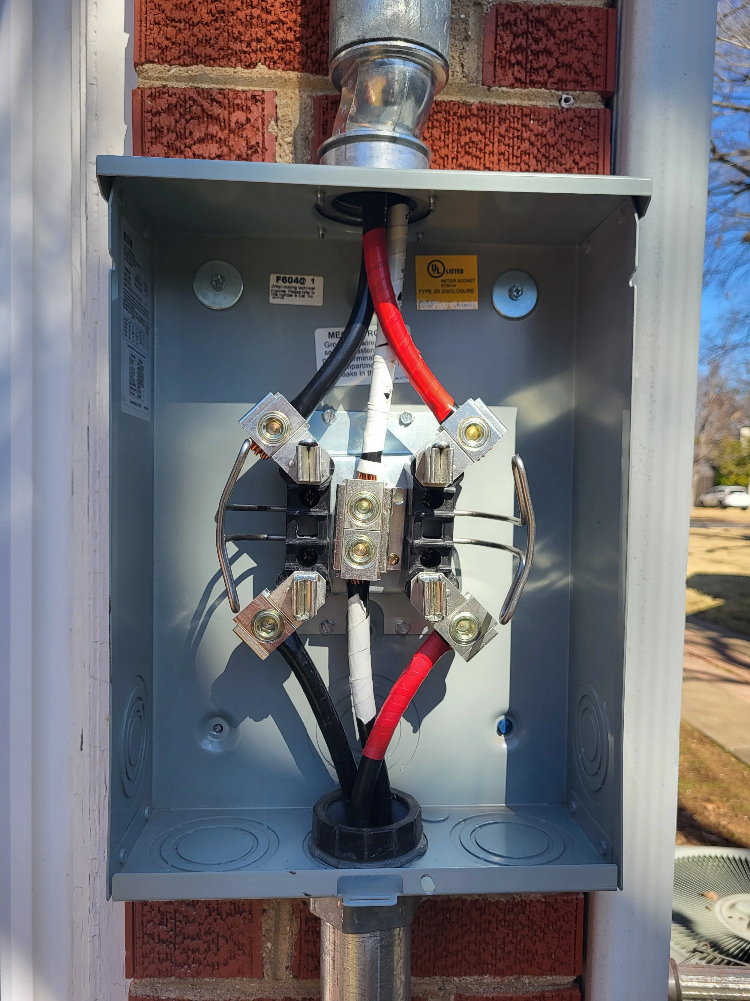 Electrical meter box with wires inside mounted on a brick wall.