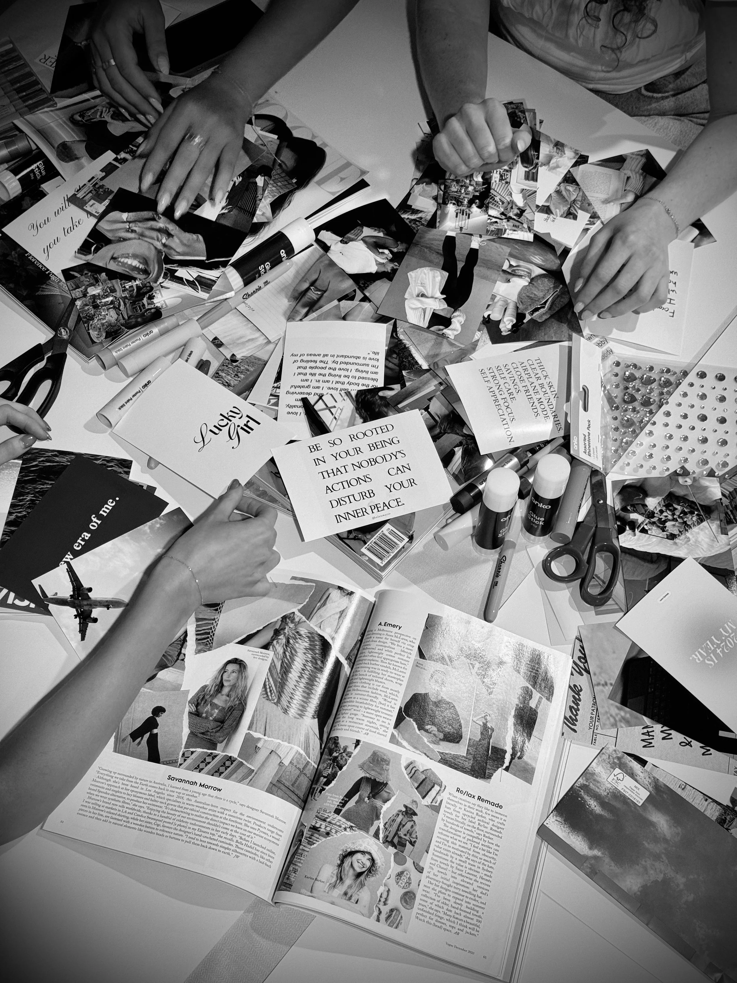 People working on a collage or scrapbook surrounded by magazines, photos, scissors, markers, and decorative stickers on a table.
