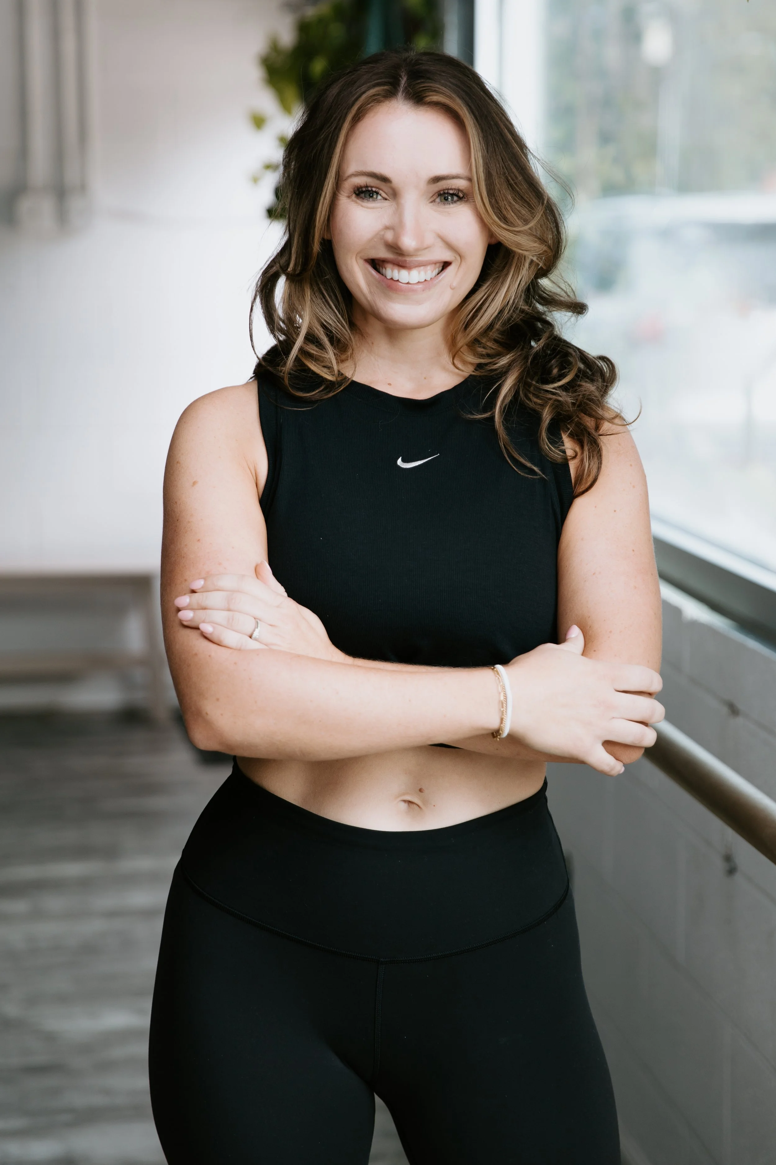 A woman with highlighted, long hair smiles for the camera. Her arms are crossed.