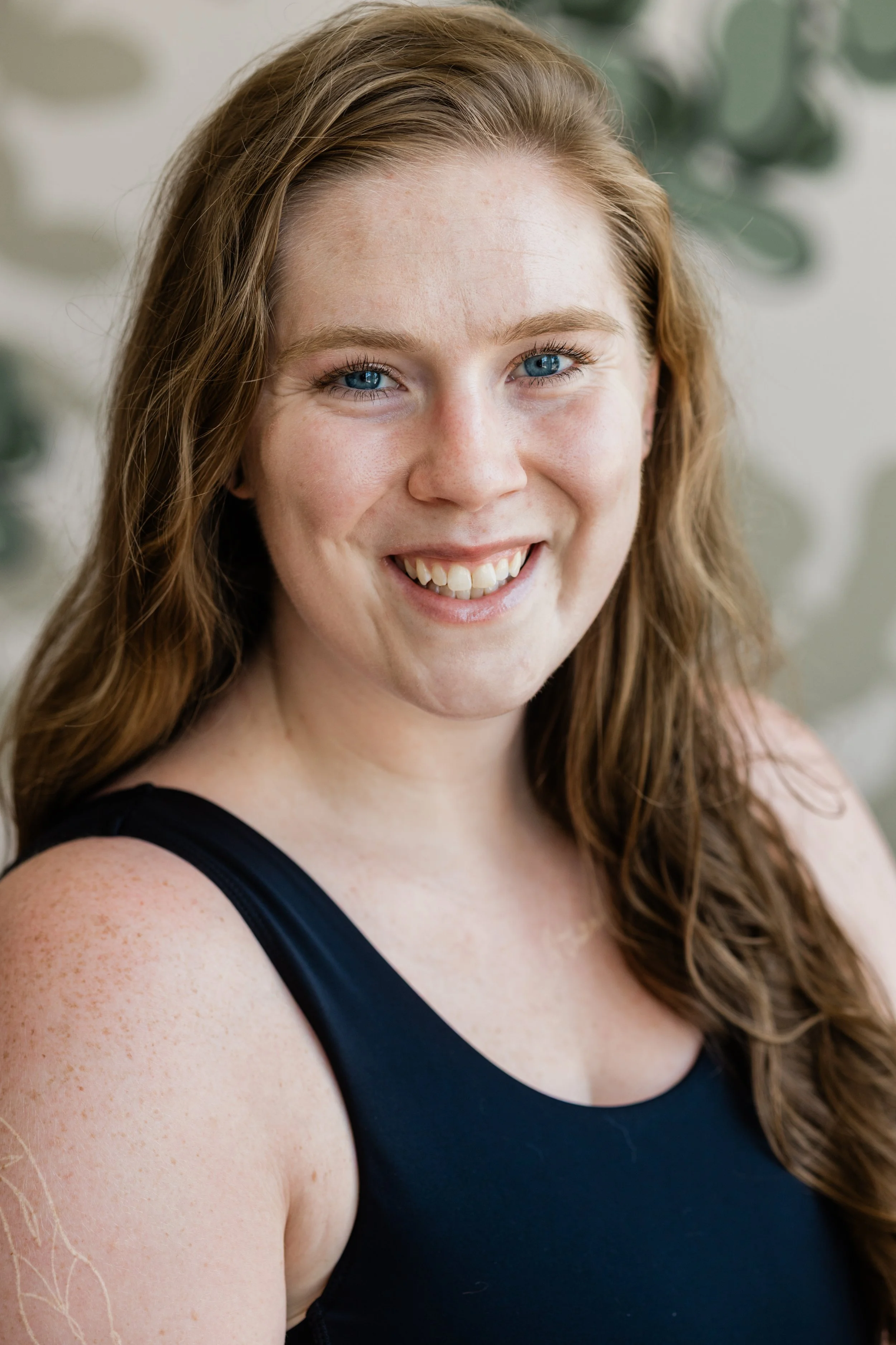 A woman with long, strawberry blonde hair smiles for the camera. She wears a black tank top.