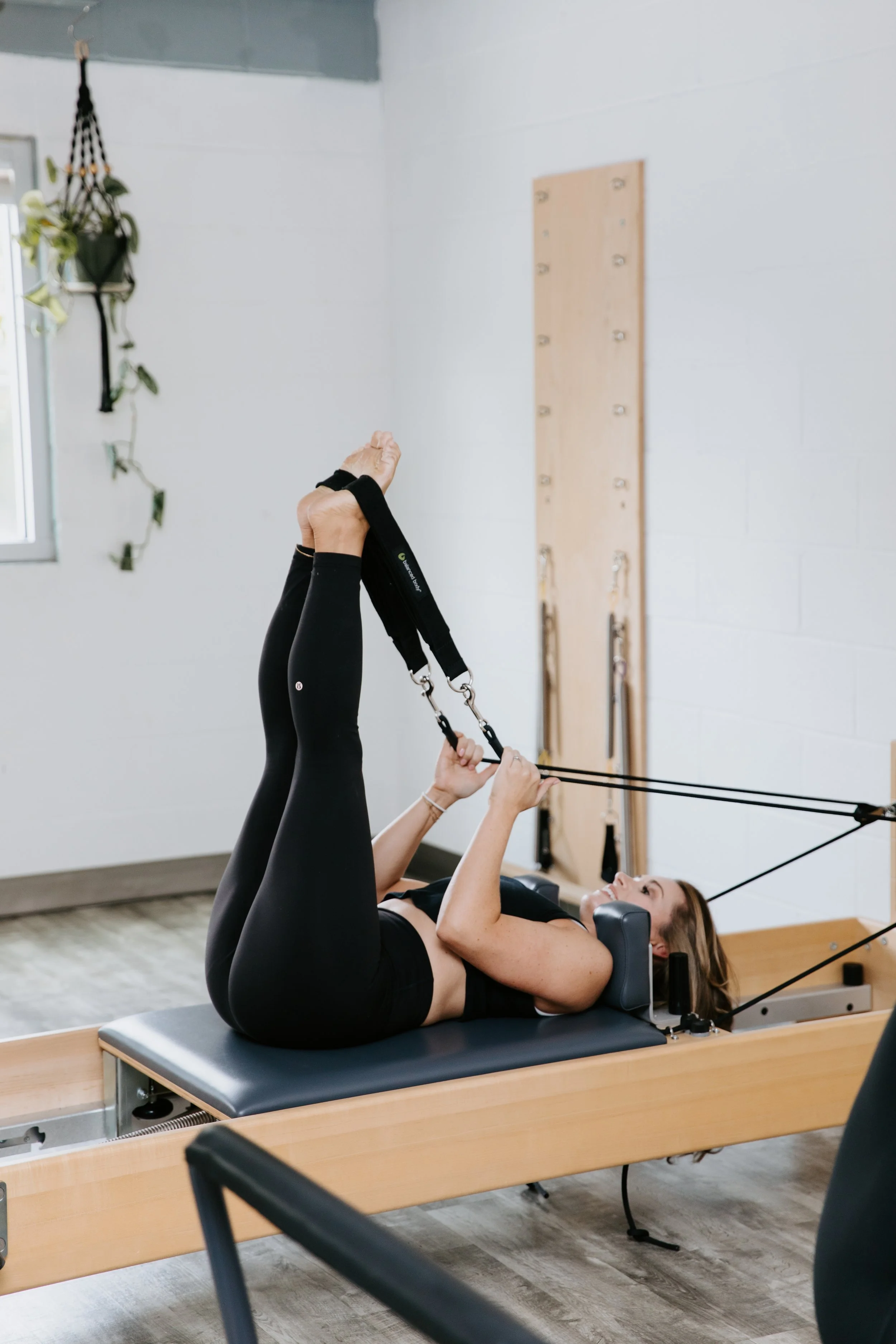 Anna practices Pilates on the Pilates reformer. Her legs are pointed up toward the ceiling and her feet are in the straps.