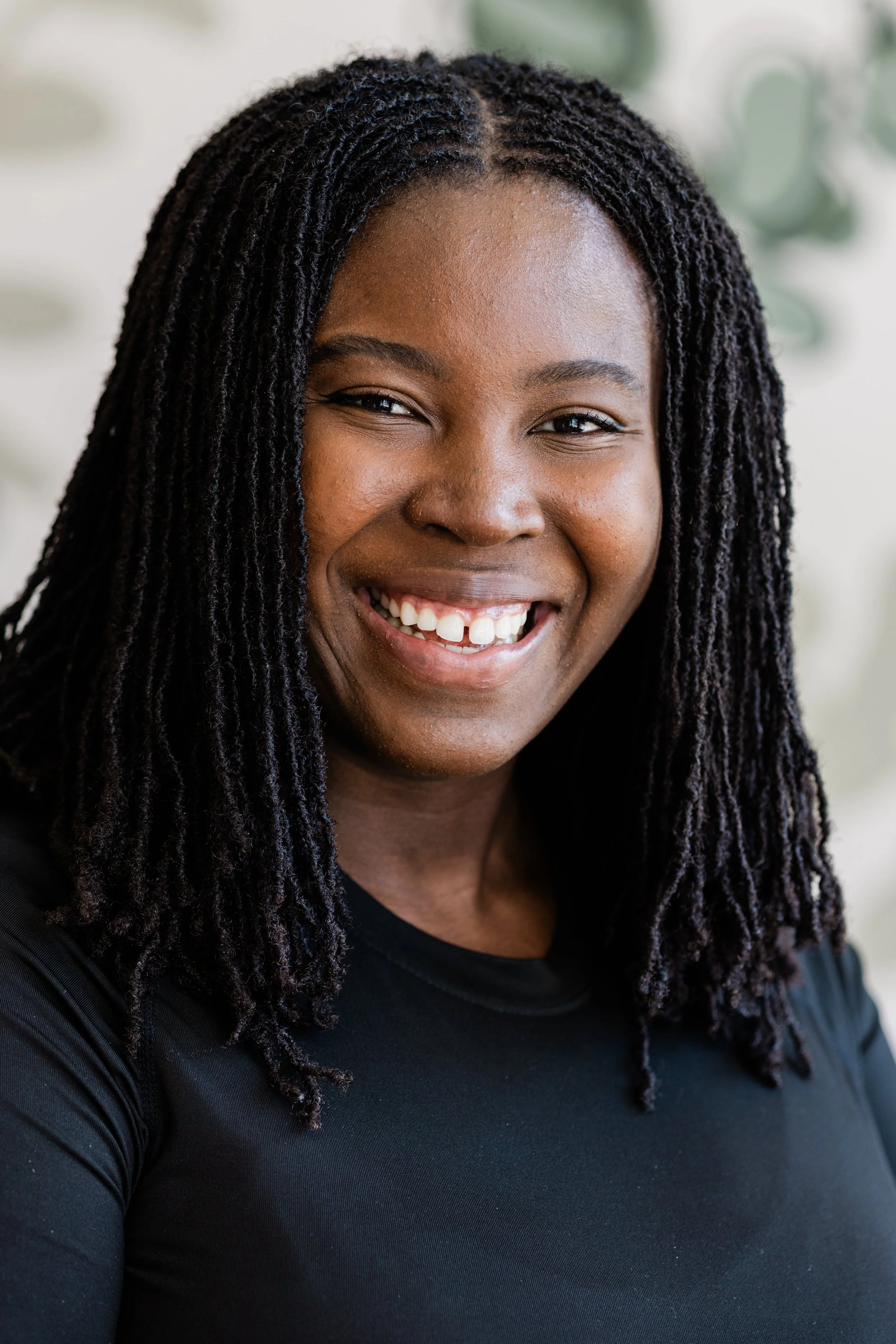A woman with medium-length black microlocs smiles for the camera. She wears a black tank top.