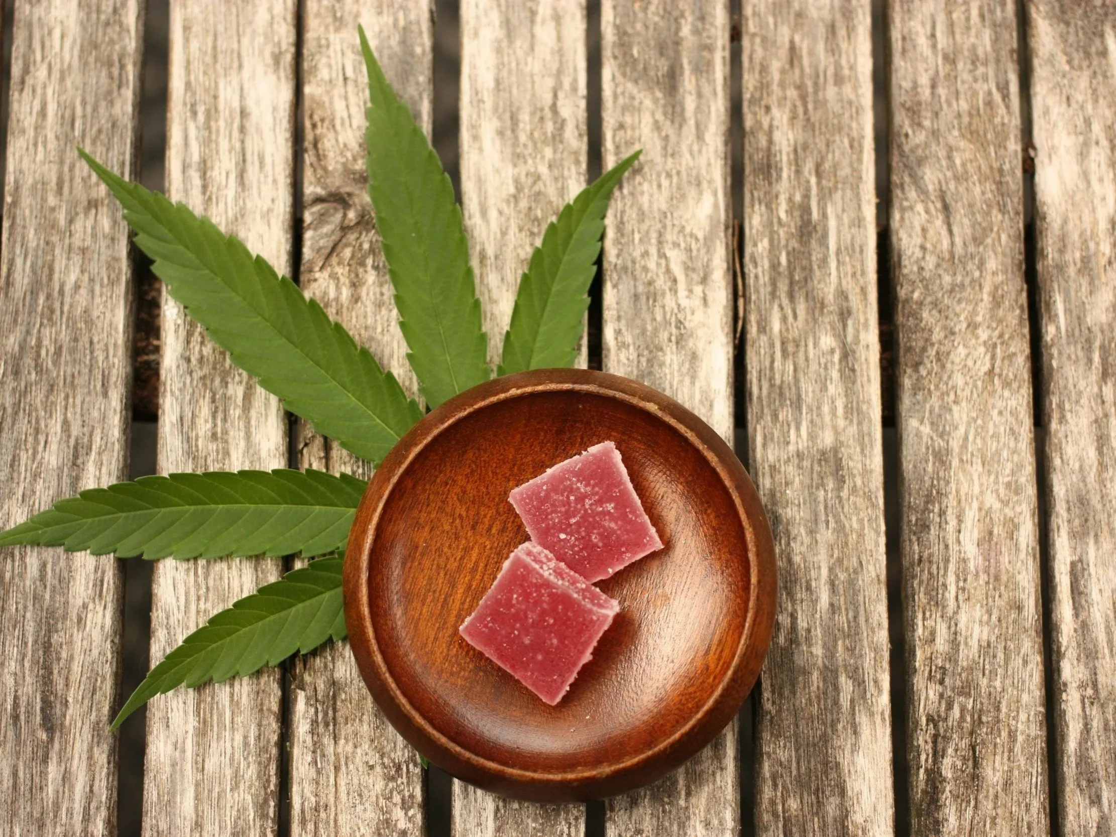 Slices of pink soap on a round wooden dish, with green leaves and a rustic wooden surface background.