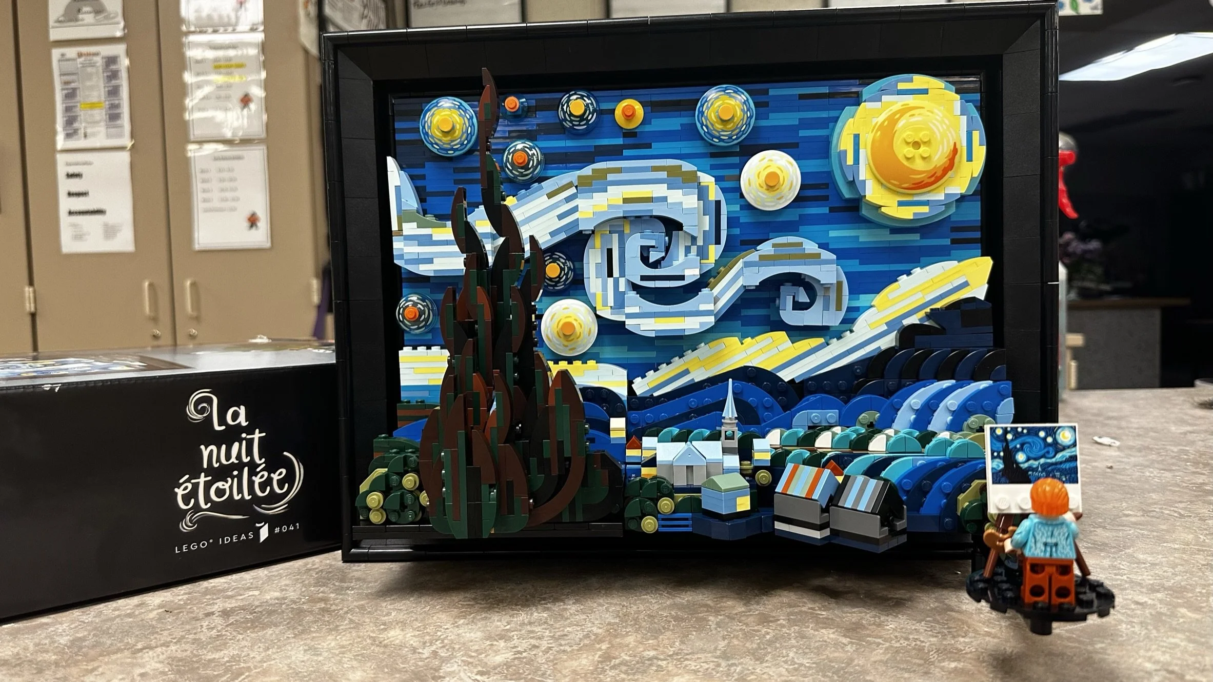 Lego mosaic of Van Gogh's Starry Night with a Lego figurine of a person in an orange hat in front.