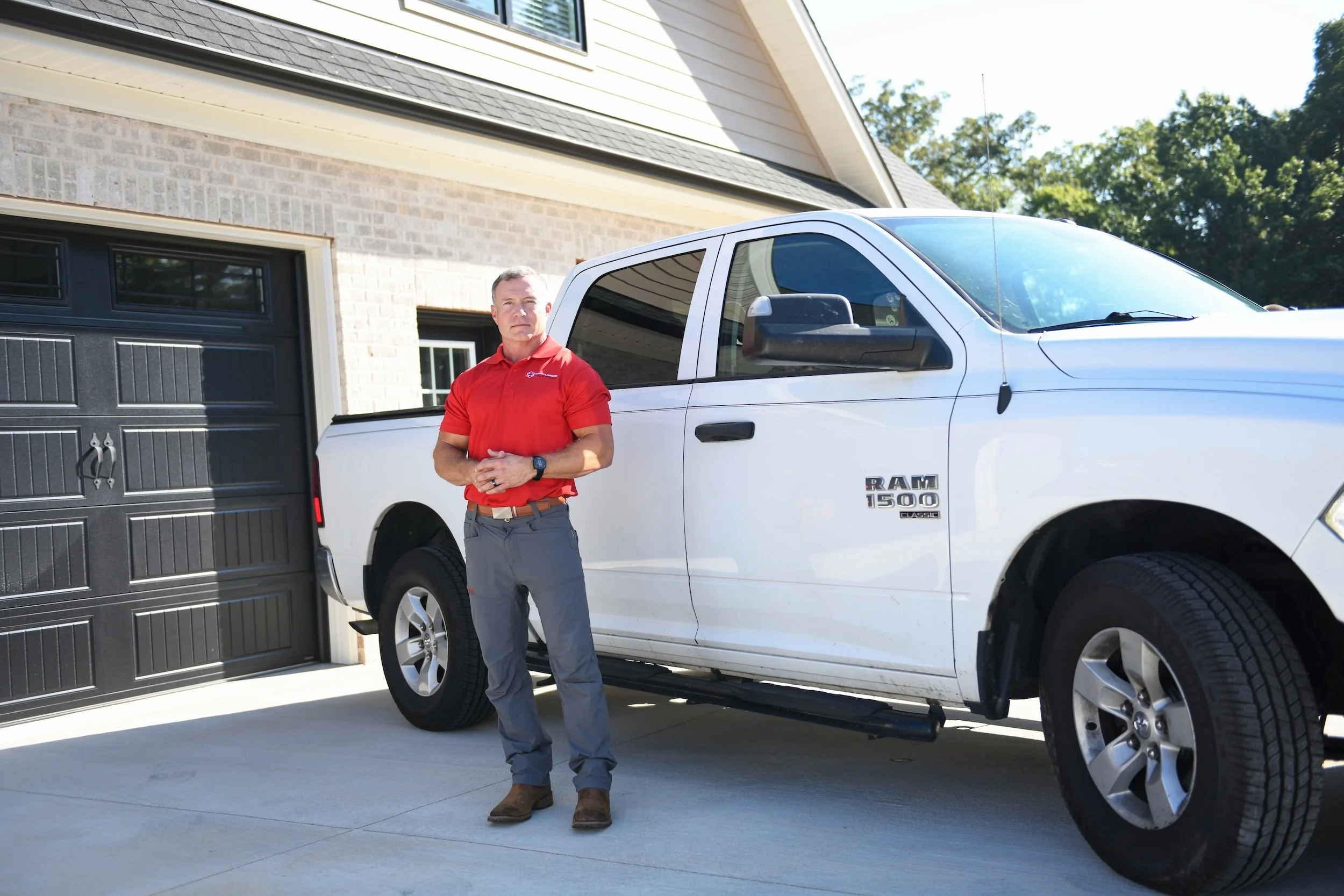 home improvement professional in a red polo beside a white pickup truck outside a modern brick house