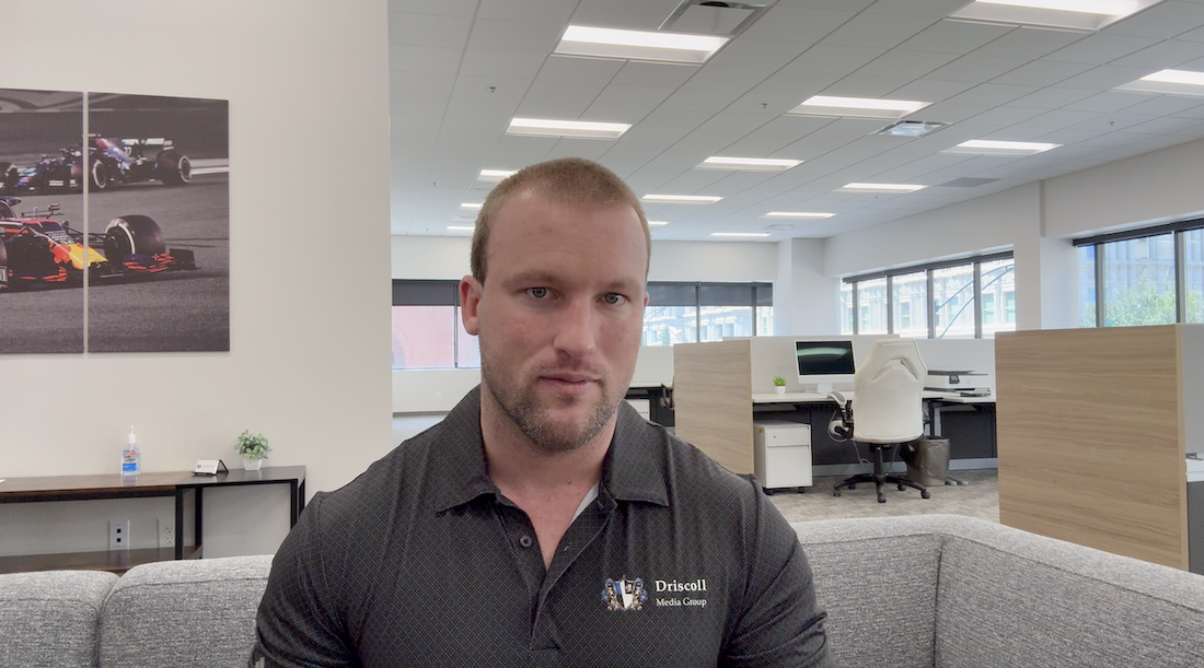 Thomas the founder of Driscoll Media Group wearing a branded polo seated in a modern office space