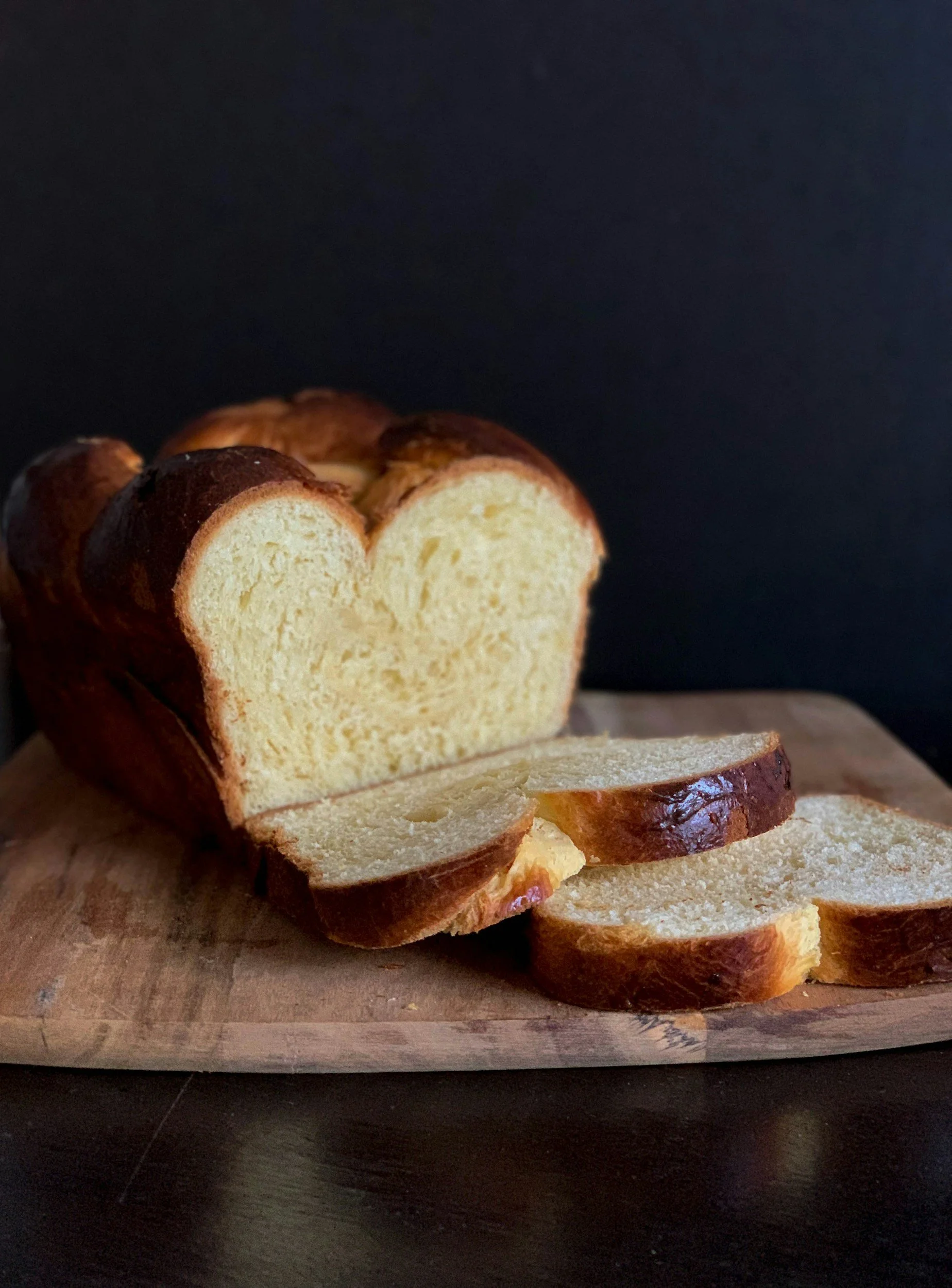 A loaf of bread with a heart-shaped cut, partially sliced on a wooden cutting board against a dark background.