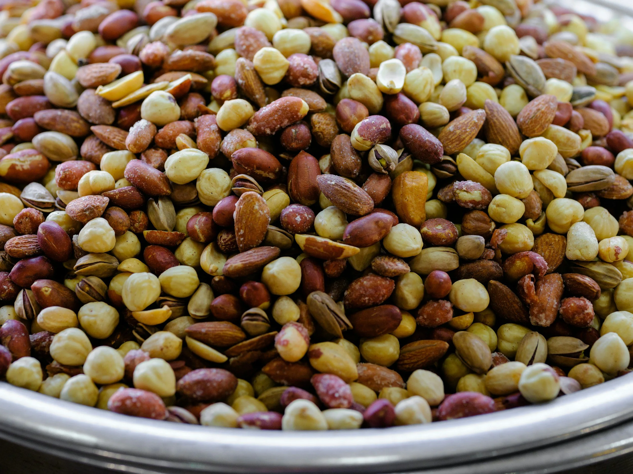 Close-up of mixed raw nuts in a metal bowl, including hazelnuts, almonds, and cashews.