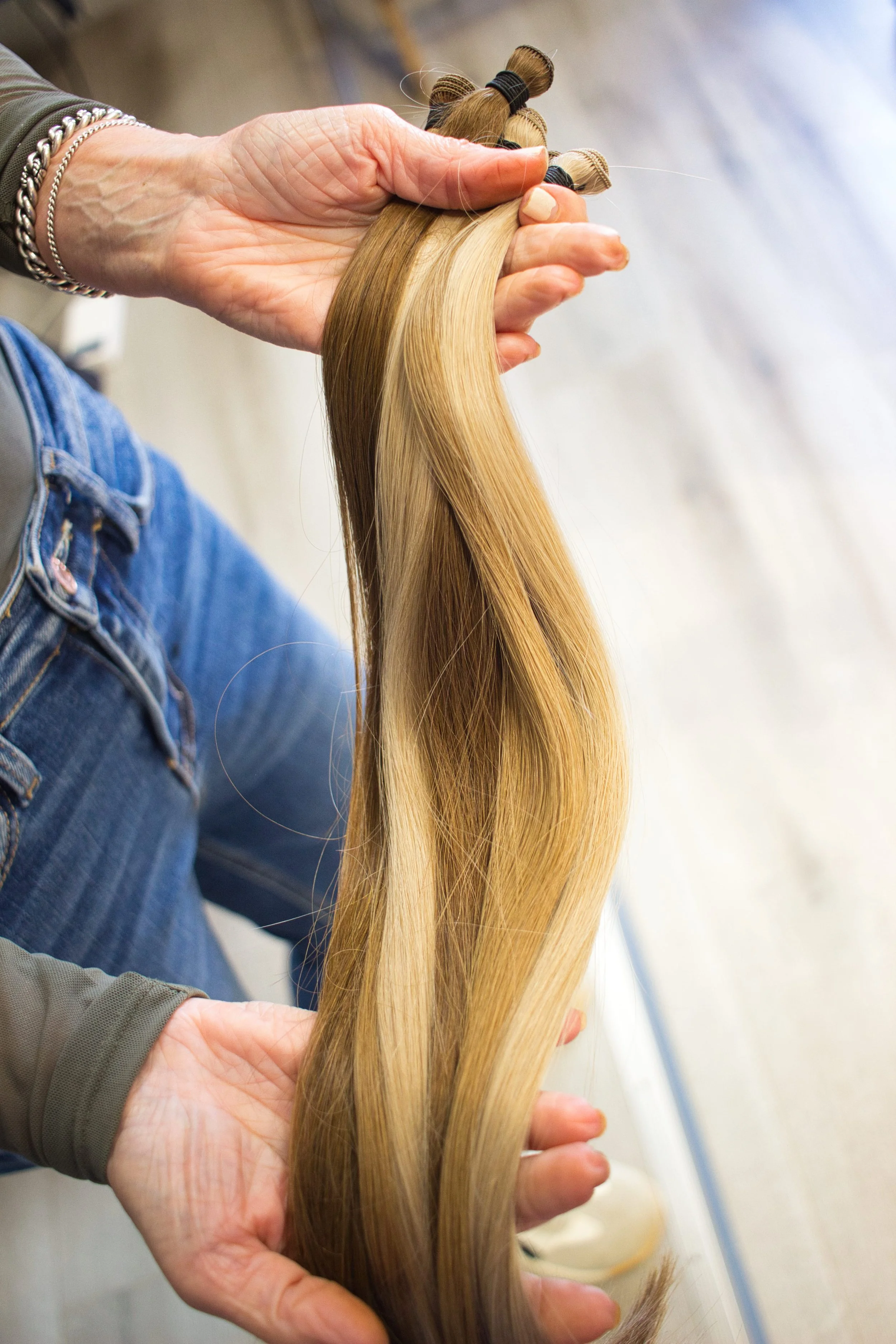 Person holding a bundle of blonde hair extensions, inspecting or preparing them.