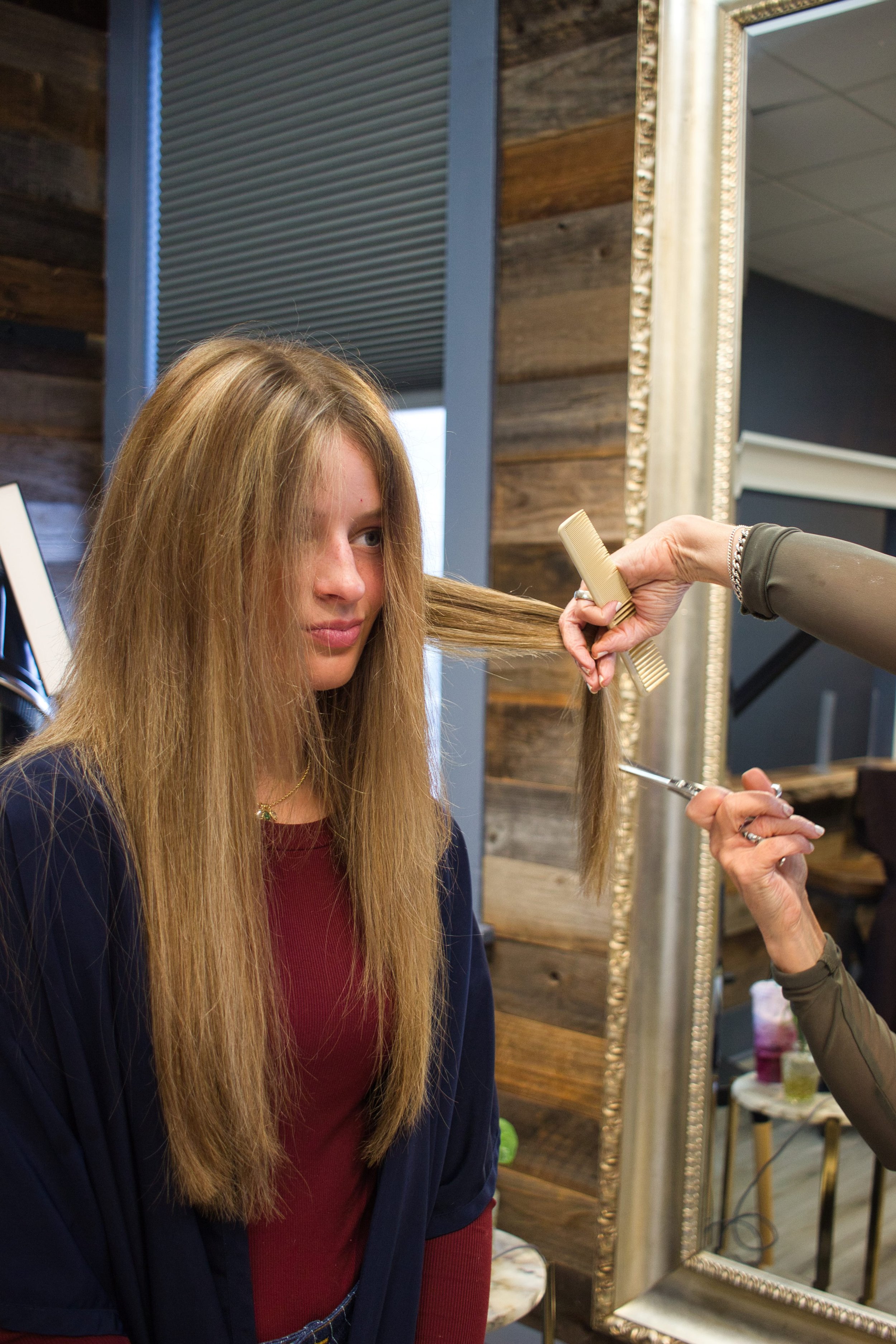 A woman with long blonde hair sitting in a salon chair while a stylist combs her hair.
