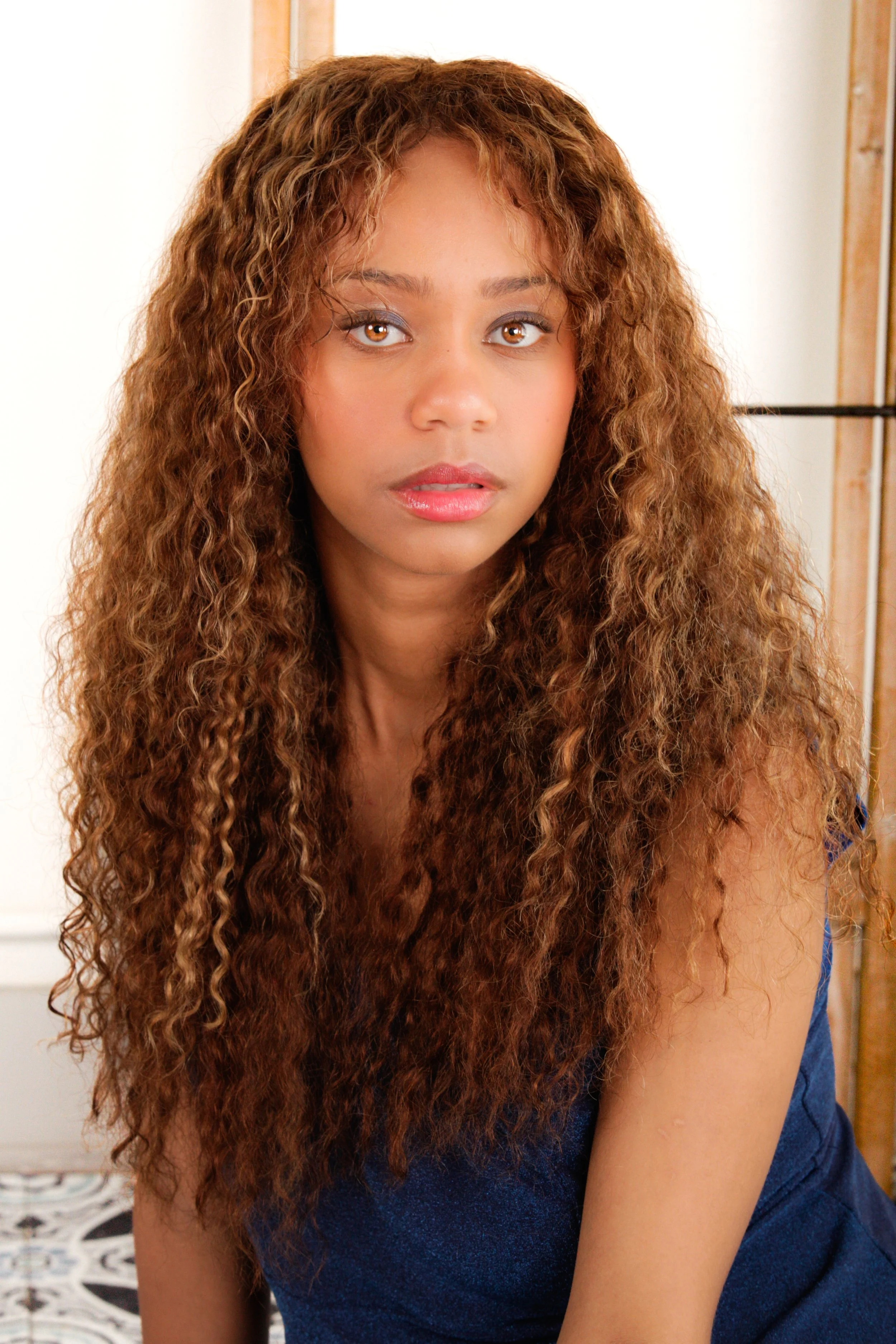 A woman with long, curly brown hair and light brown eyes looking directly at the camera.