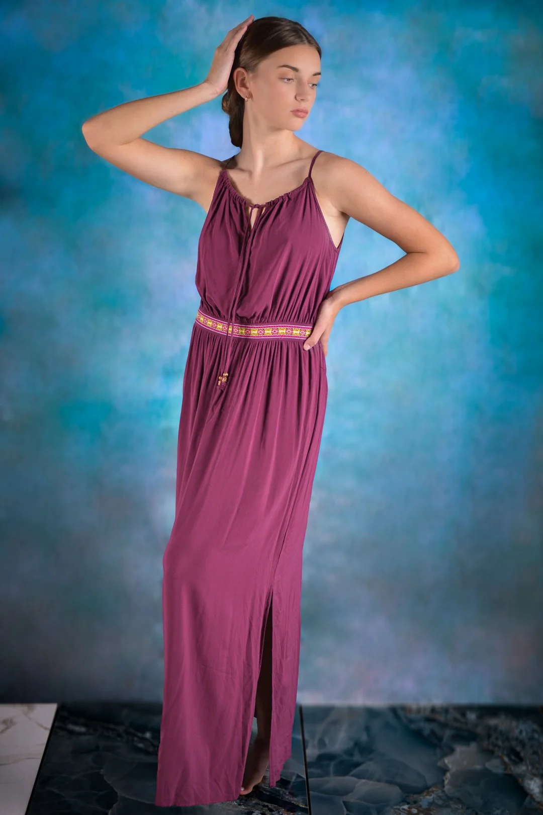 A young woman in a purple maxi dress standing against a colorful, textured backdrop.