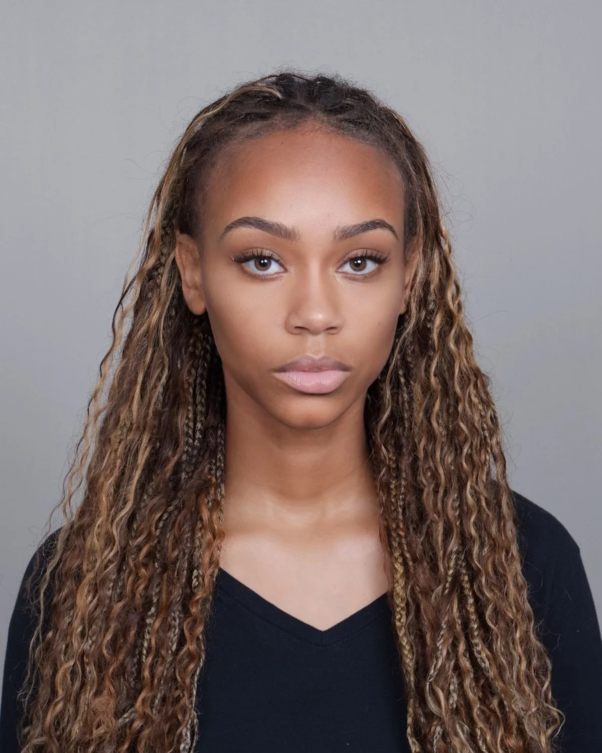 A woman with long, curly hair and a serious expression, wearing a black top, against a plain gray background.