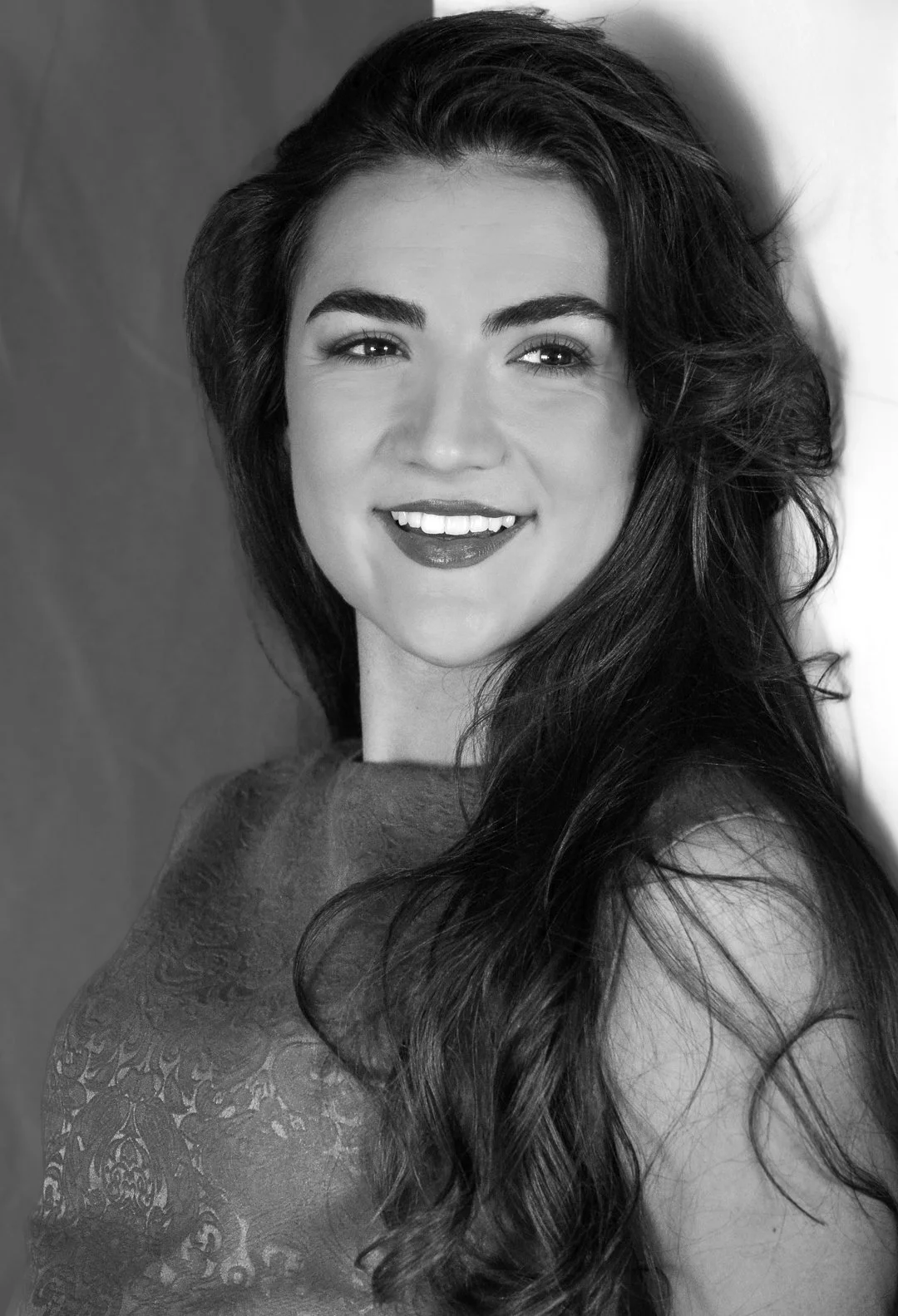 Black and white portrait of a woman with long, wavy hair smiling and looking at the camera.
