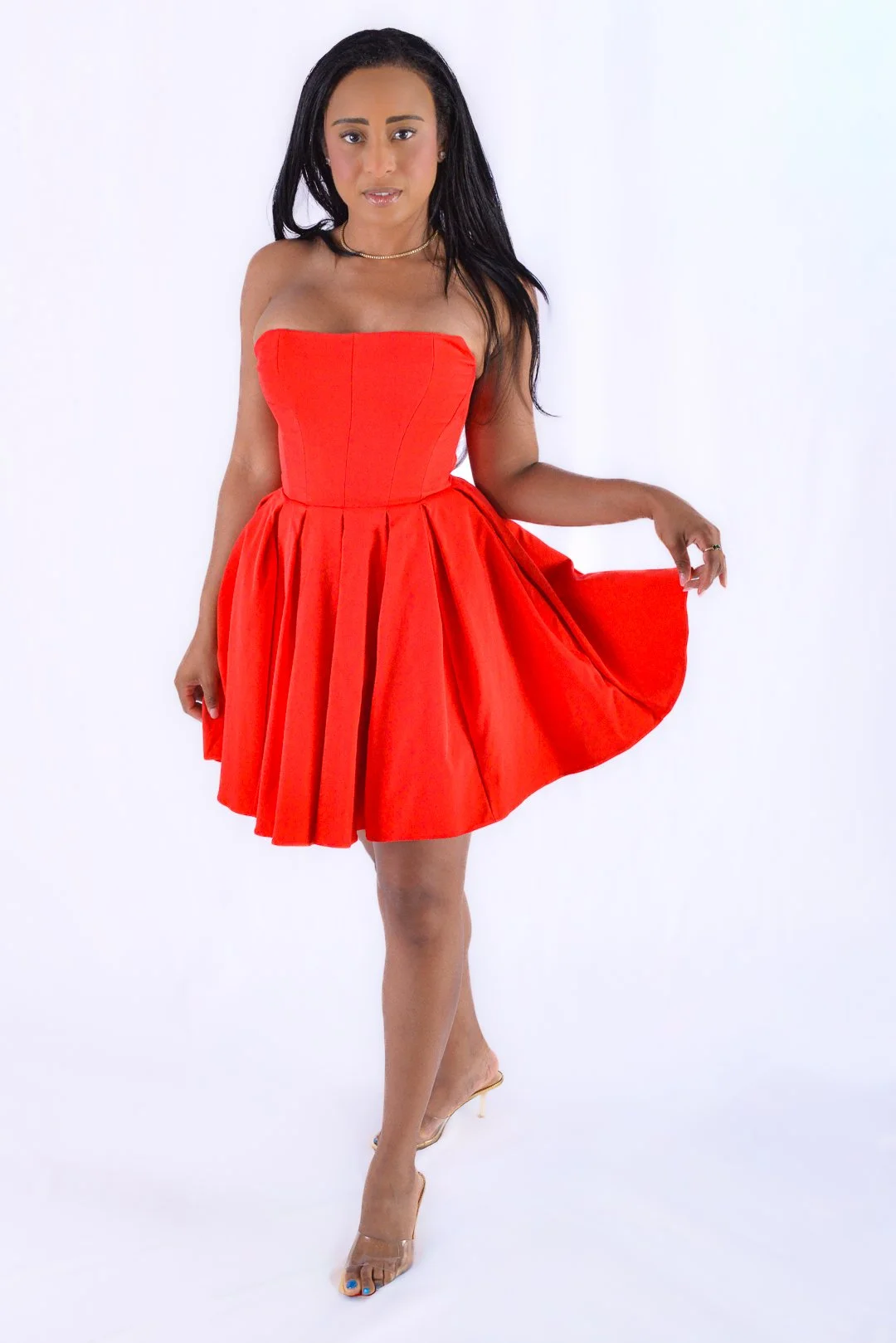 Woman in a strapless red dress holding the hem of her skirt, standing on a white background.