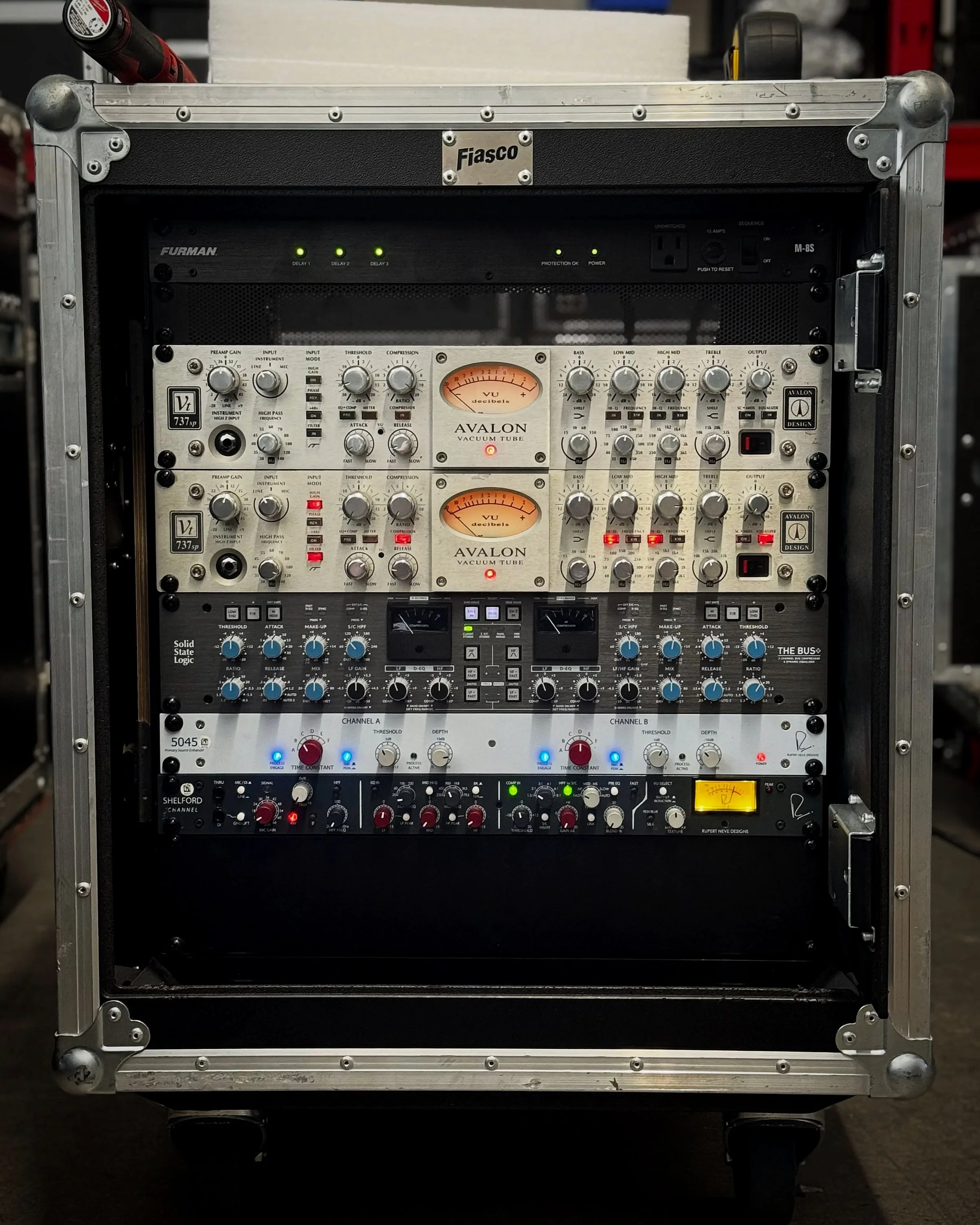 A rack-mounted audio equipment case with various audio processing and mixing gear, including Avalon vacuum tube units, digital controls, and level meters.