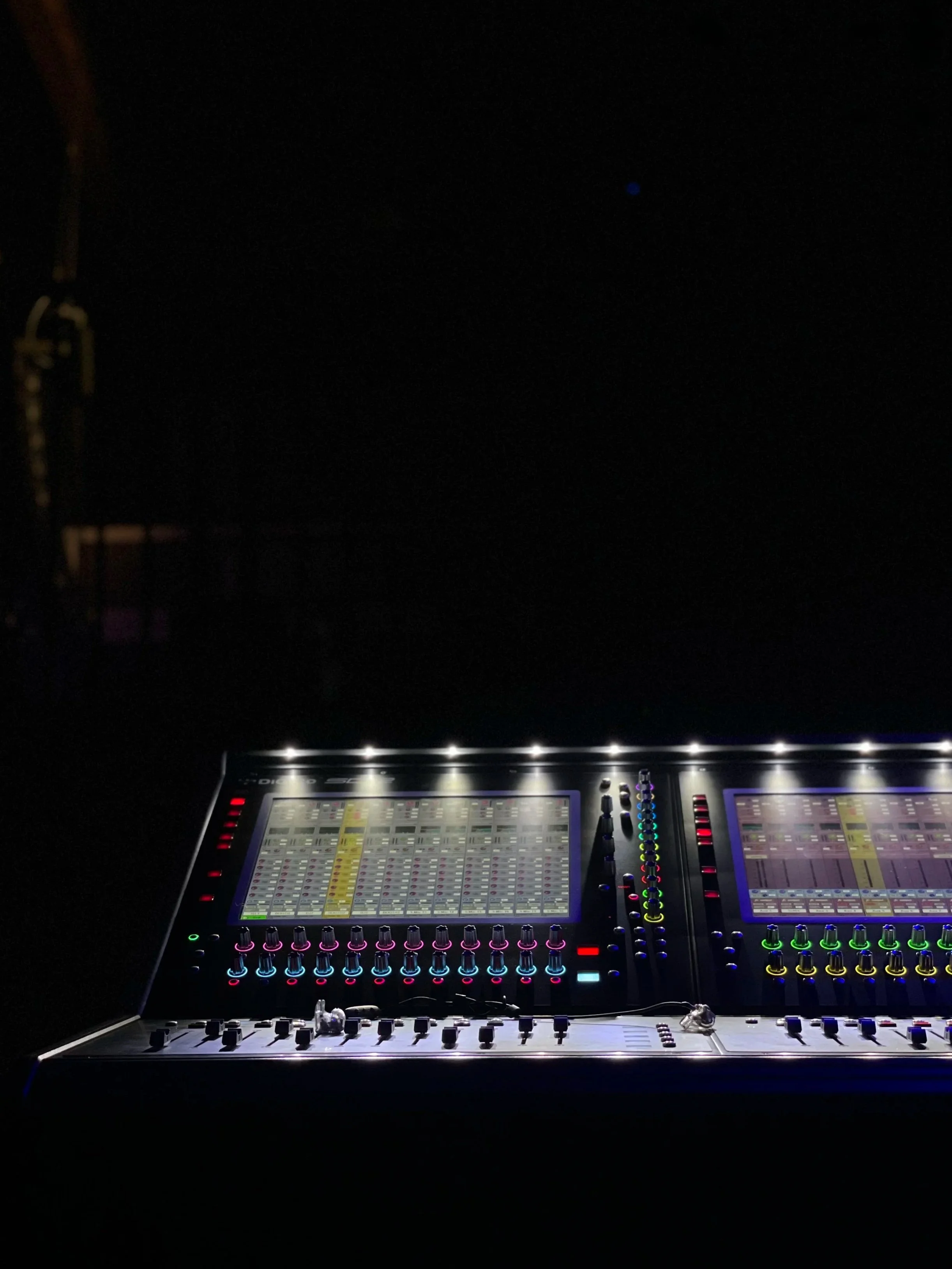 A DiGiCO SD12 digital audio mixing console with illuminated controls and screens, set against a dark background.