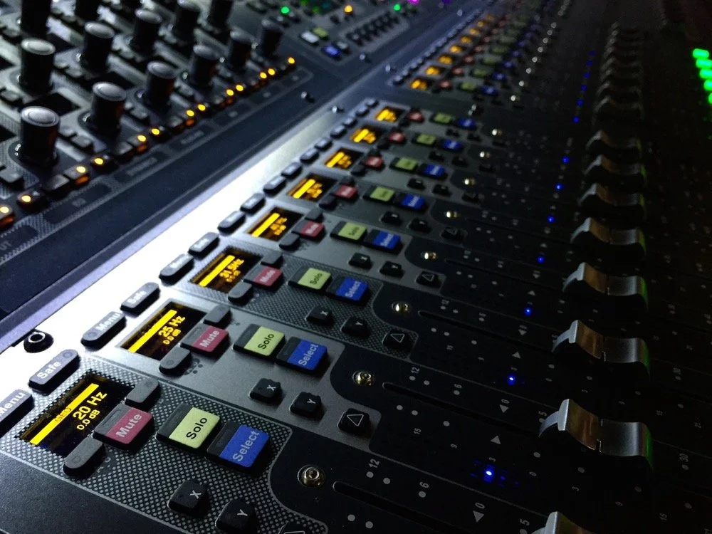 Close-up of a professional audio mixing console with illuminated buttons and faders.