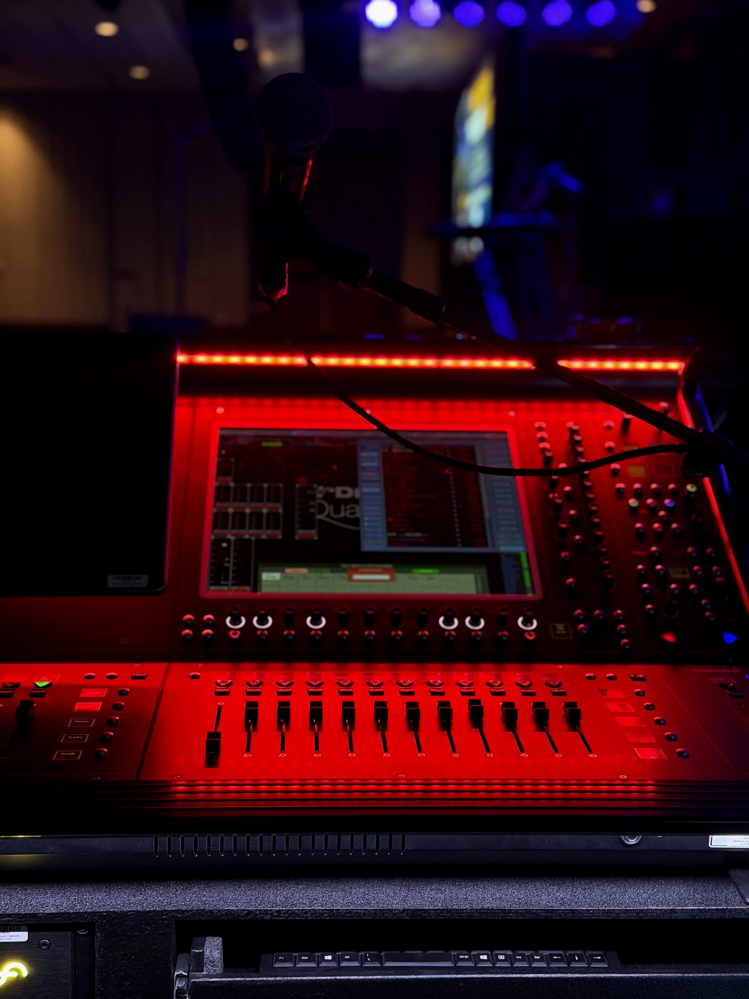 Mixing console with a microphone in a dark performance venue, illuminated by red LED lights.