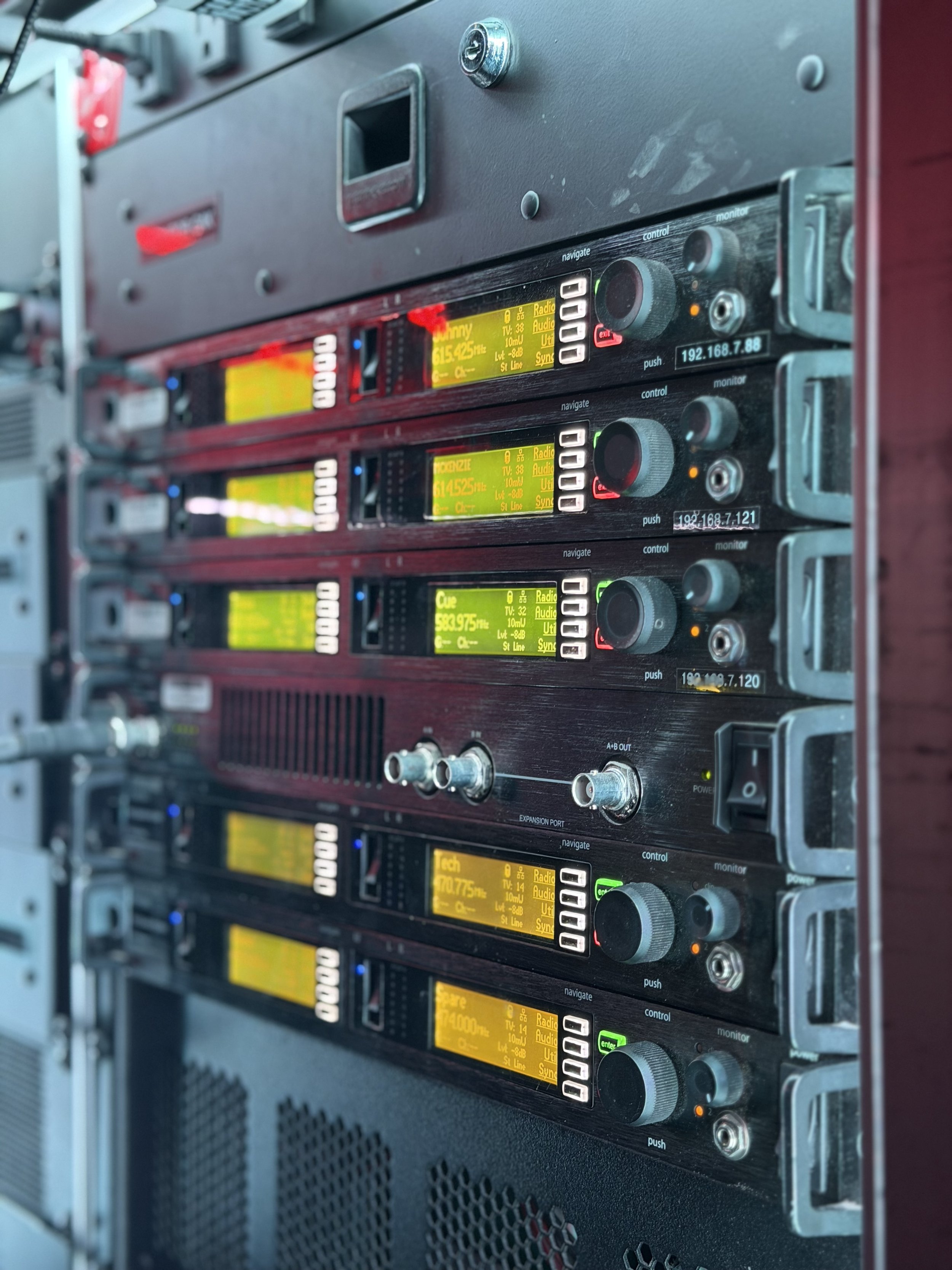 Server rack with multiple electronic communication devices, each with a yellow display and various buttons, knobs, and ports