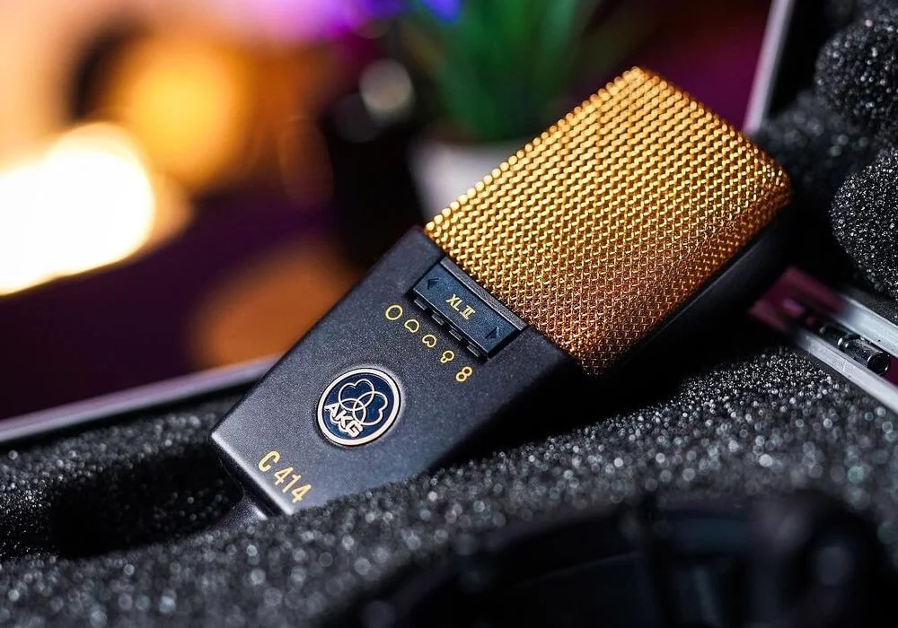 Close-up of a AKG C414 microphone with a gold mesh grille, placed on black foam padding.