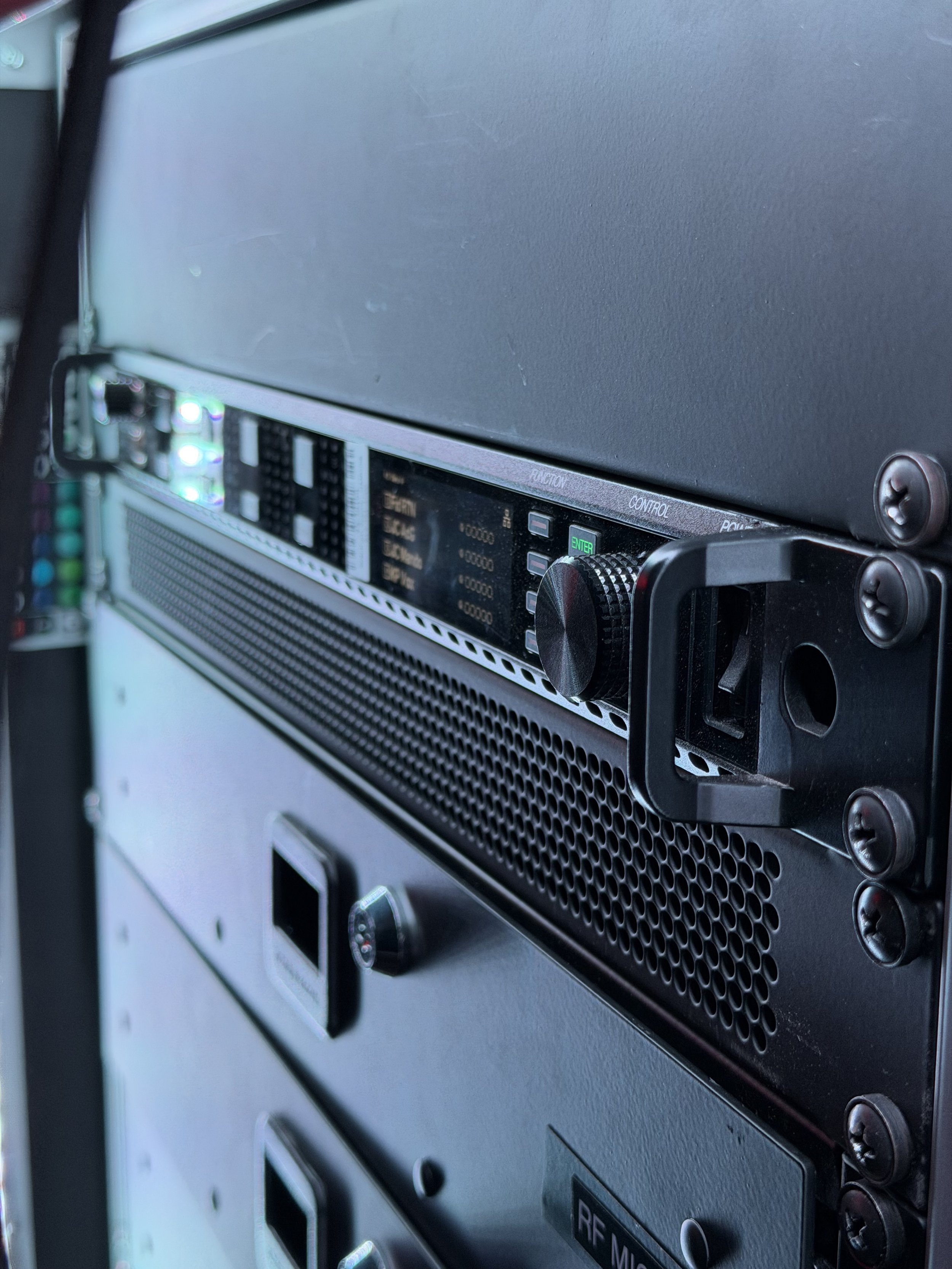 Close-up of a professional microphone receiver in a rack, with controls, knobs, and digital display, mounted inside a black metal case with screws.