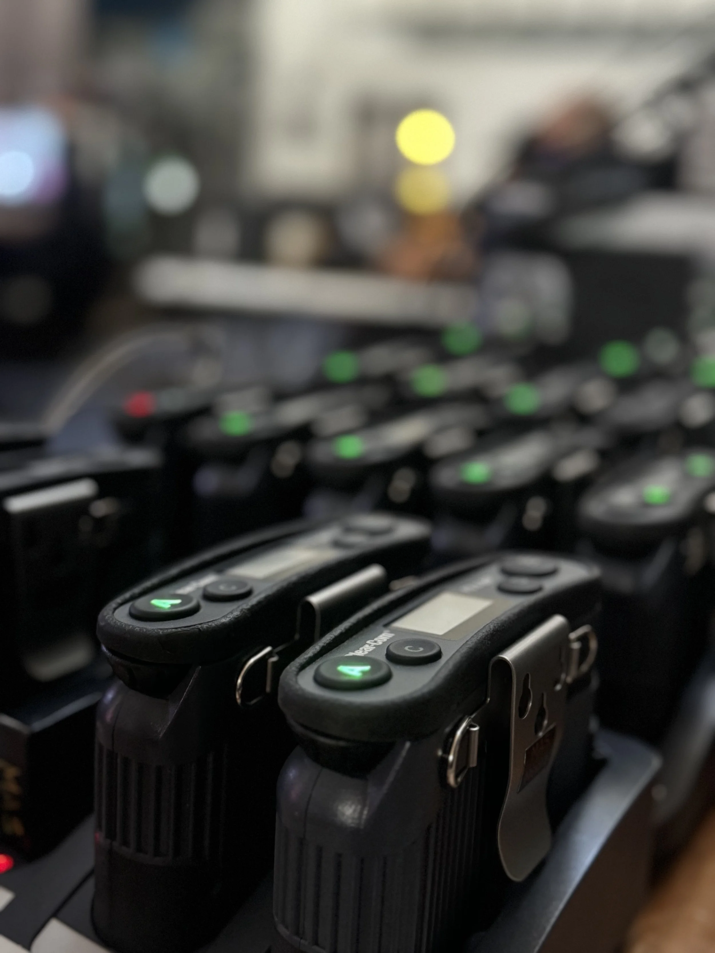 Close-up of multiple black wireless microphones with green indicator lights, placed on a DJ or sound mixing console with blurred background.