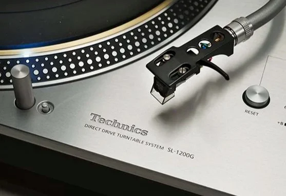 Close-up of a Technics SL-1200G turntable, showing the tonearm, control knobs, and part of the platter.