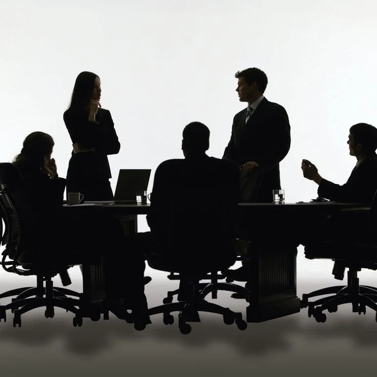 Silhouettes of six business professionals in a meeting room, some standing and some sitting, with laptops and glasses of water on the table, against a plain white background.